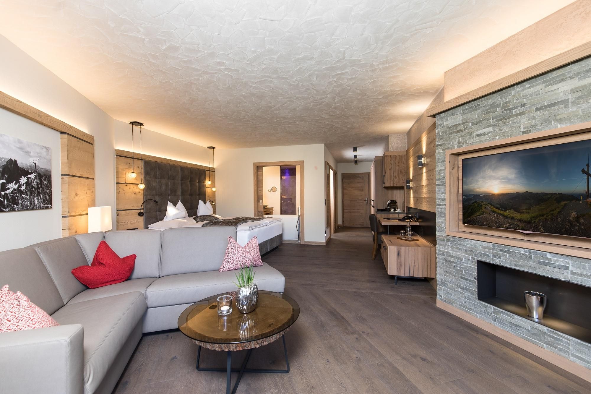 A modern room with a cozy sofa, a round table, and an open kitchen. The walls are decorated with wood and stone elements, creating a warm atmosphere.