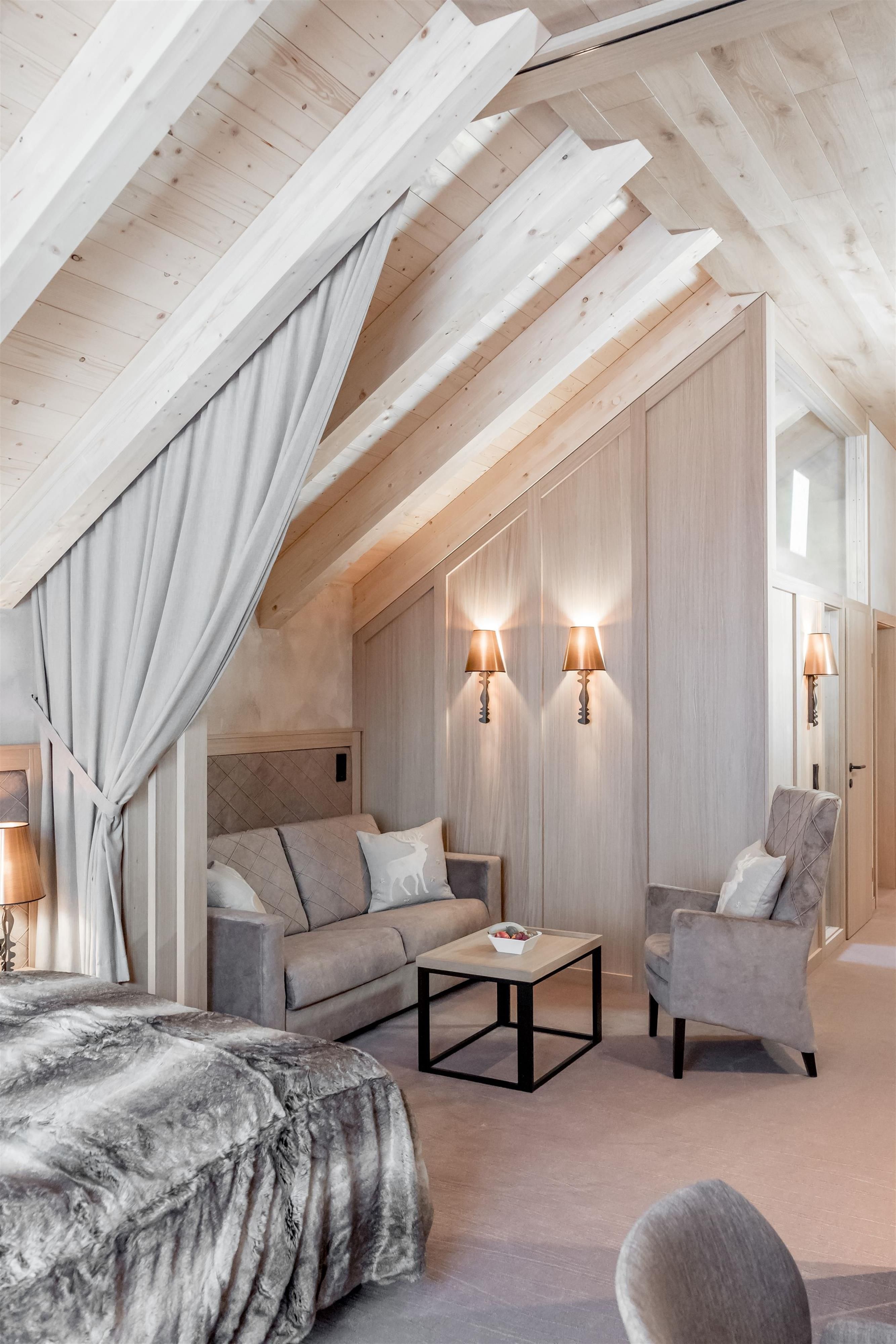 A stylish bedroom with a wooden ceiling and cozy furnishings. There is a sofa, two armchairs, and soft lighting.