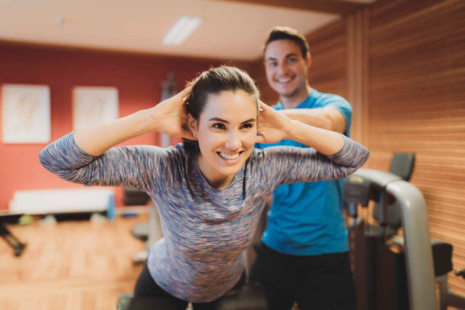 A woman is training with a coach at the gym. She is smiling and looks motivated as the coach encourages her.