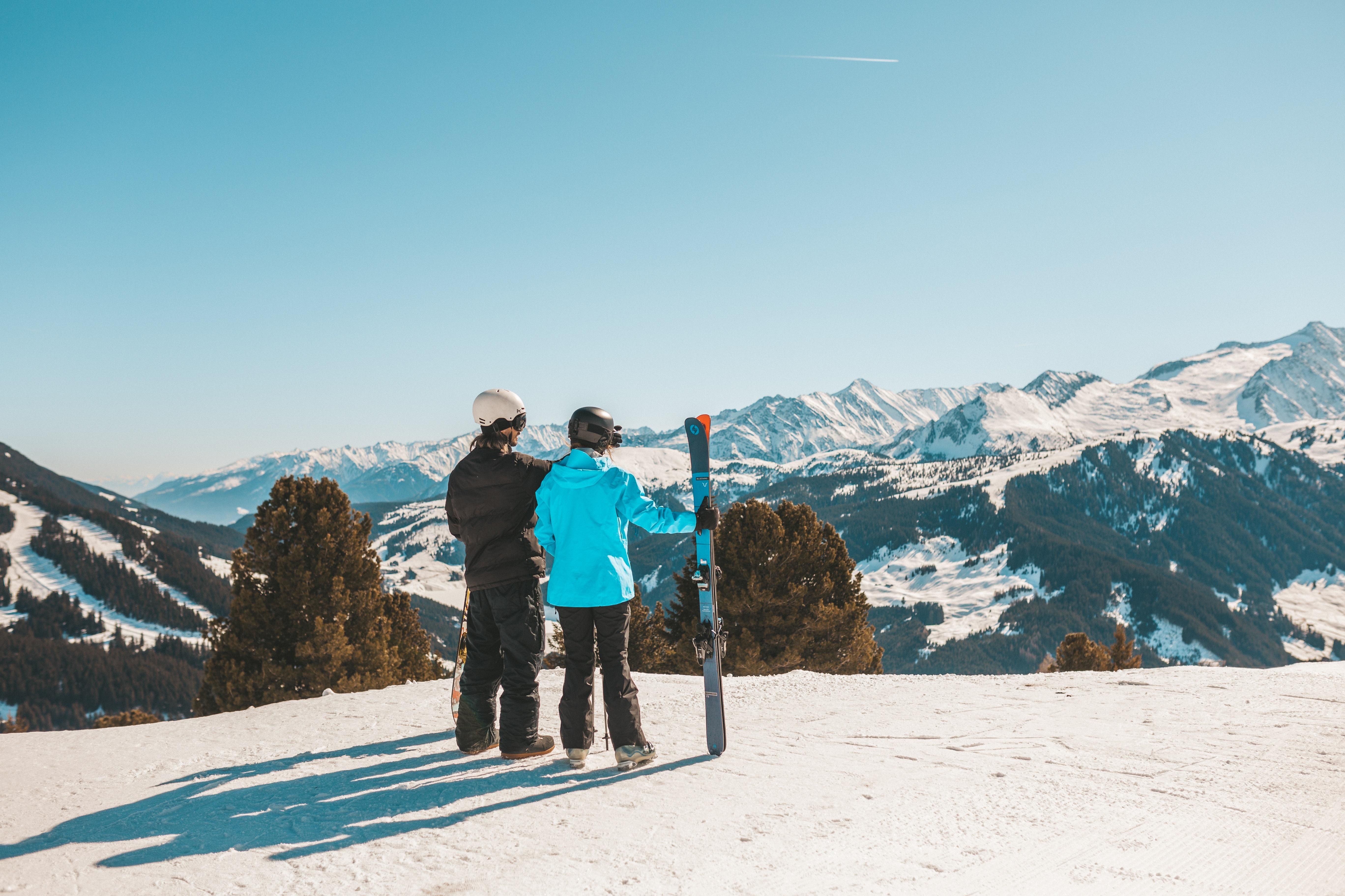 Two children are standing on a snow-covered mountain and looking at the snowy mountains in the distance. It is a clear, sunny day.