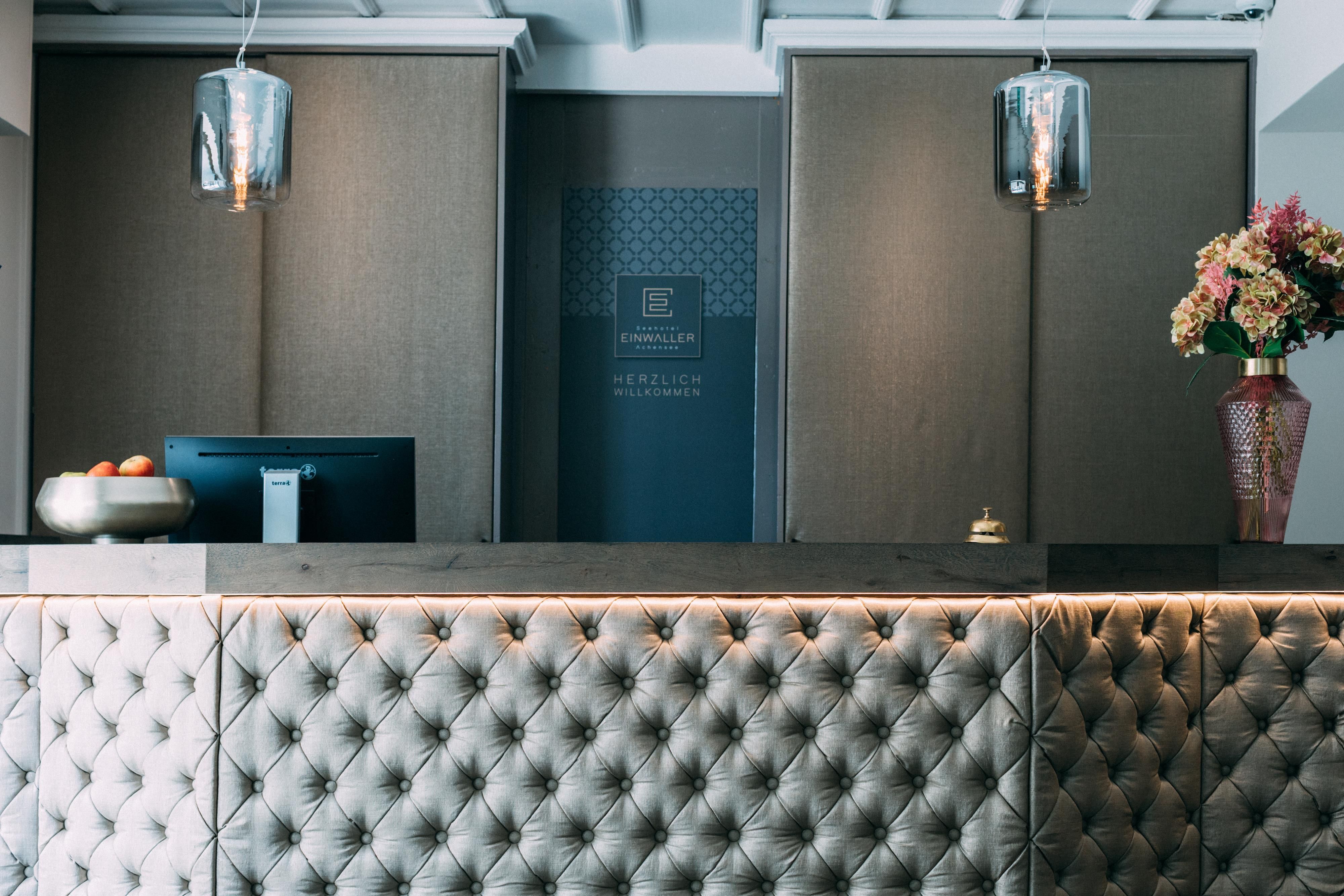 An elegant reception area with a upholstered reception desk. In the background, stylish lamps and fresh flowers are visible.