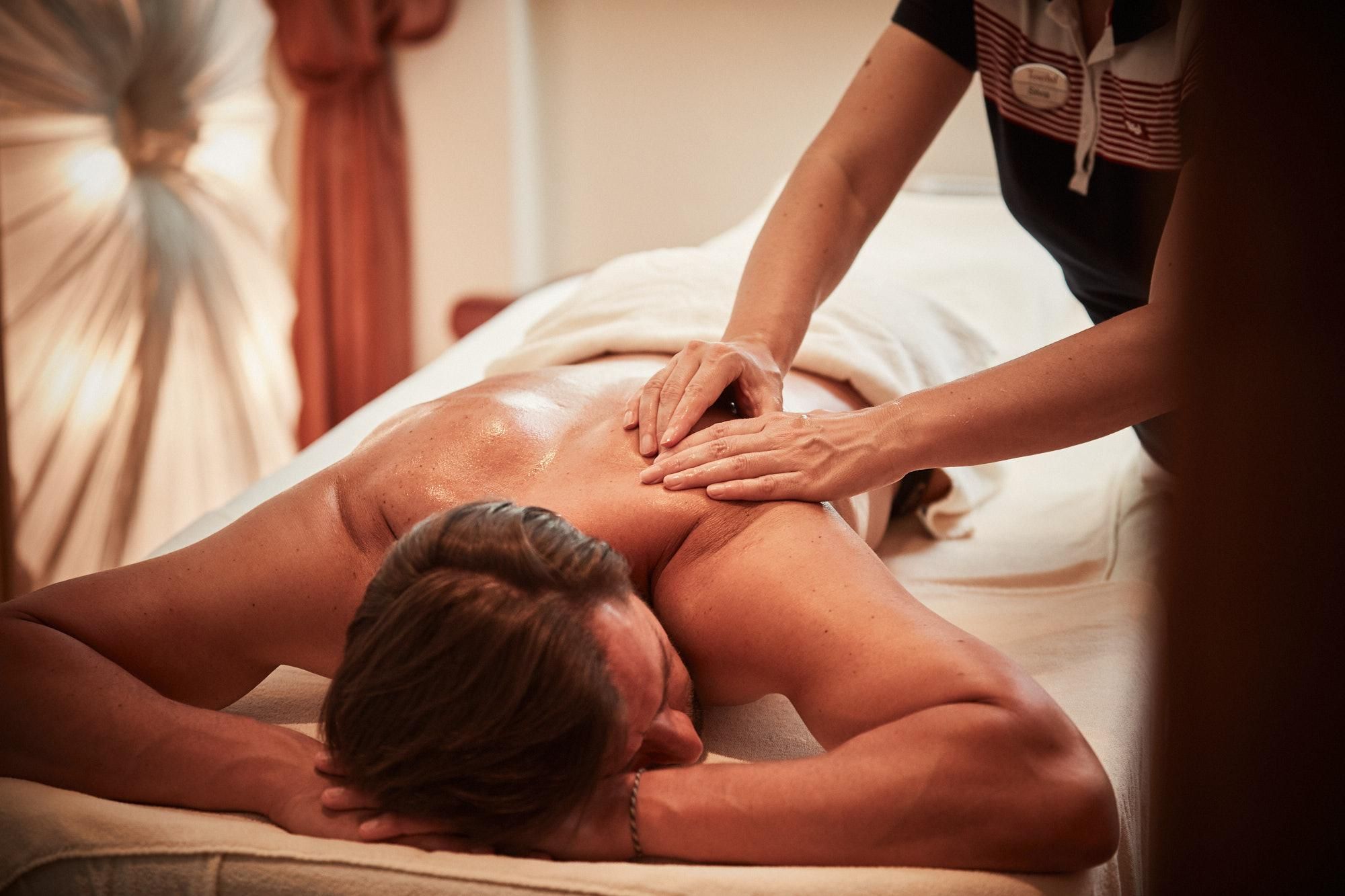A relaxing massage in a tranquil environment. One person lies on a couch while another gently massages their shoulders.