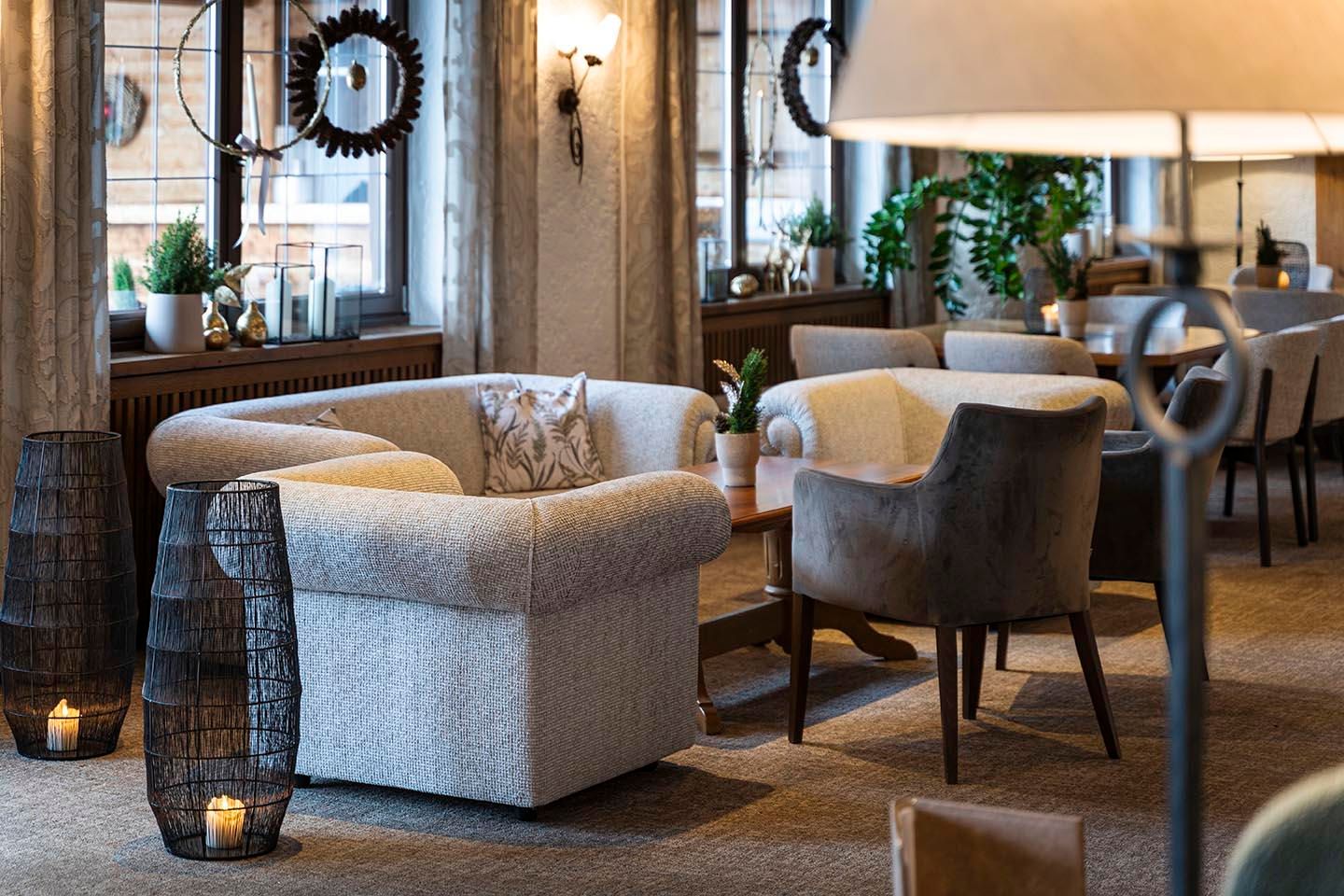 A cozy lounge area with comfortable armchairs and a bright, inviting ambiance. Large windows offer a view of the outdoor area, while plants add a fresh touch.