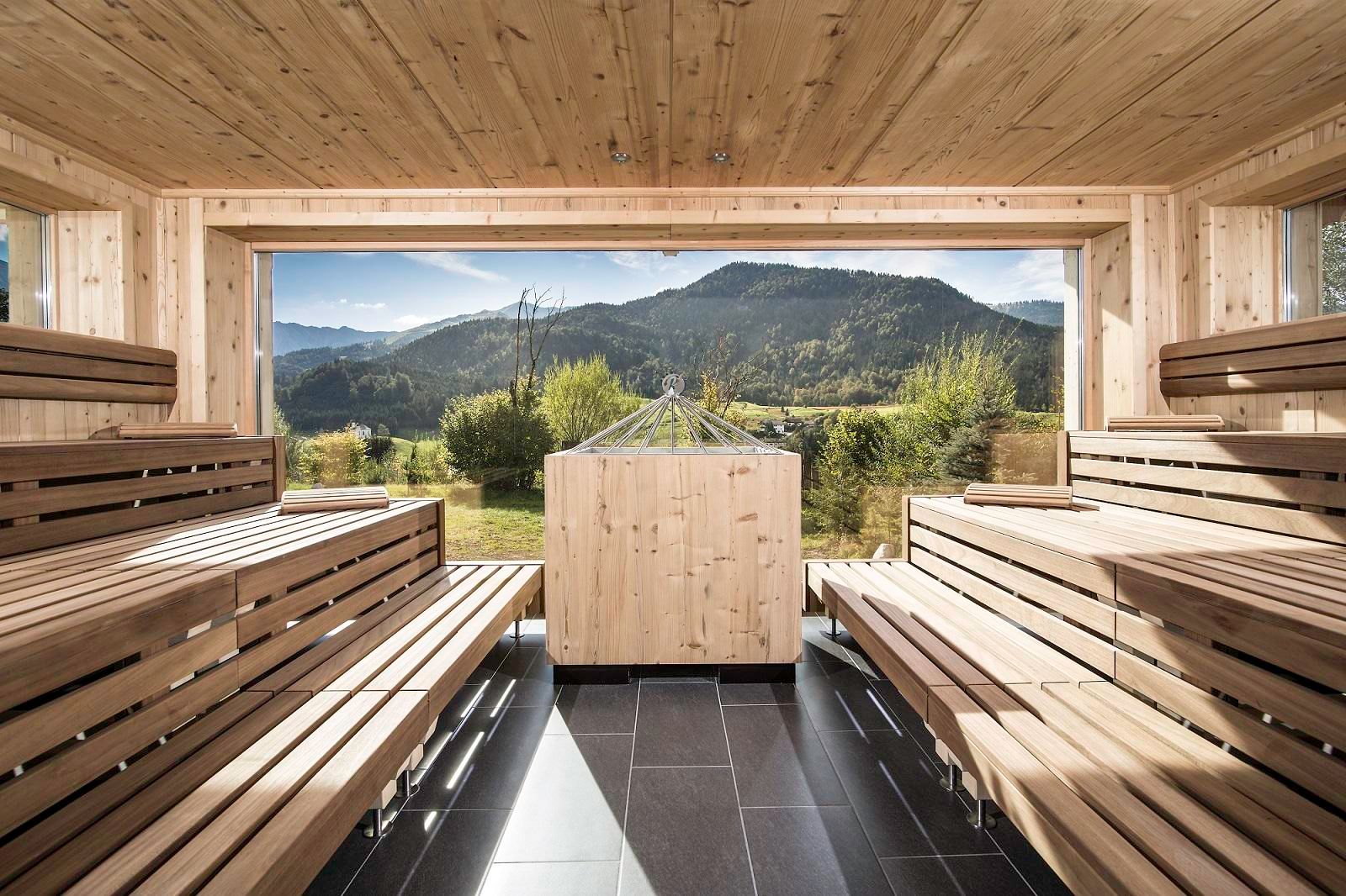A modern sauna area made of light wood with a view of the mountains. Large windows let in plenty of light and offer a beautiful view of nature.