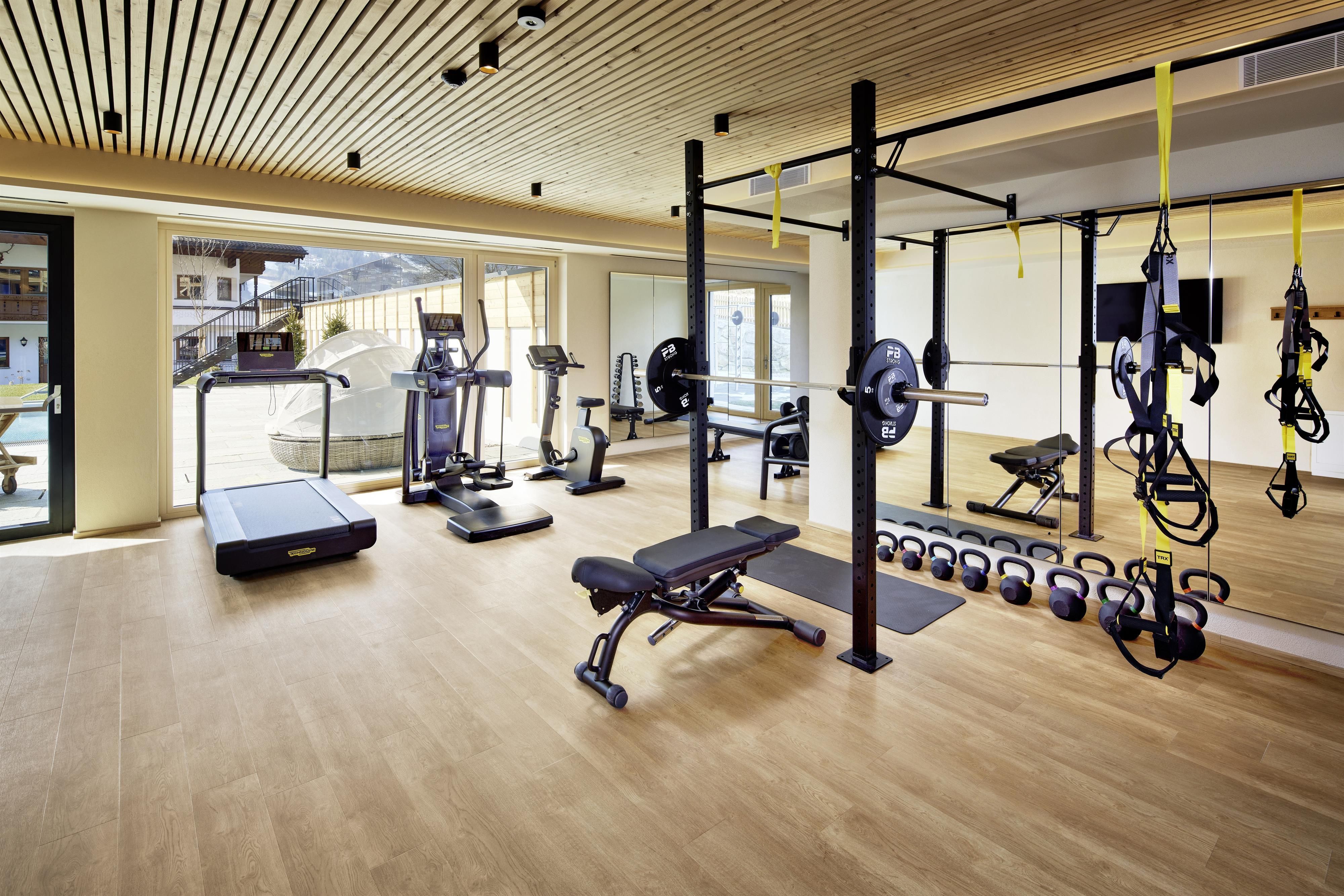 A modern fitness room with various training equipment. The room has large windows that provide plenty of daylight.