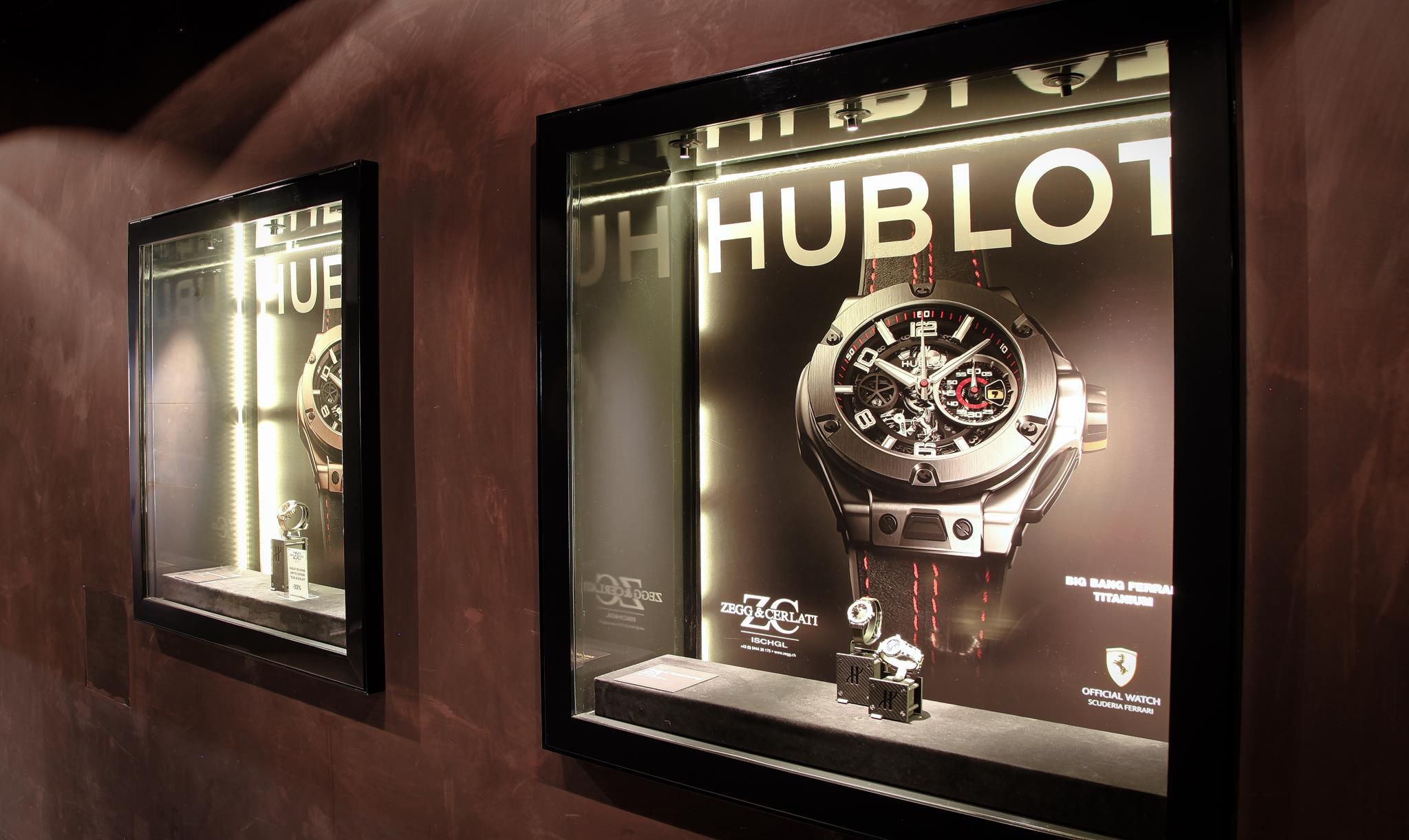 Two illuminated display cases showcase high-quality watches from the brand Hublot. The background is designed to be dark and elegant.