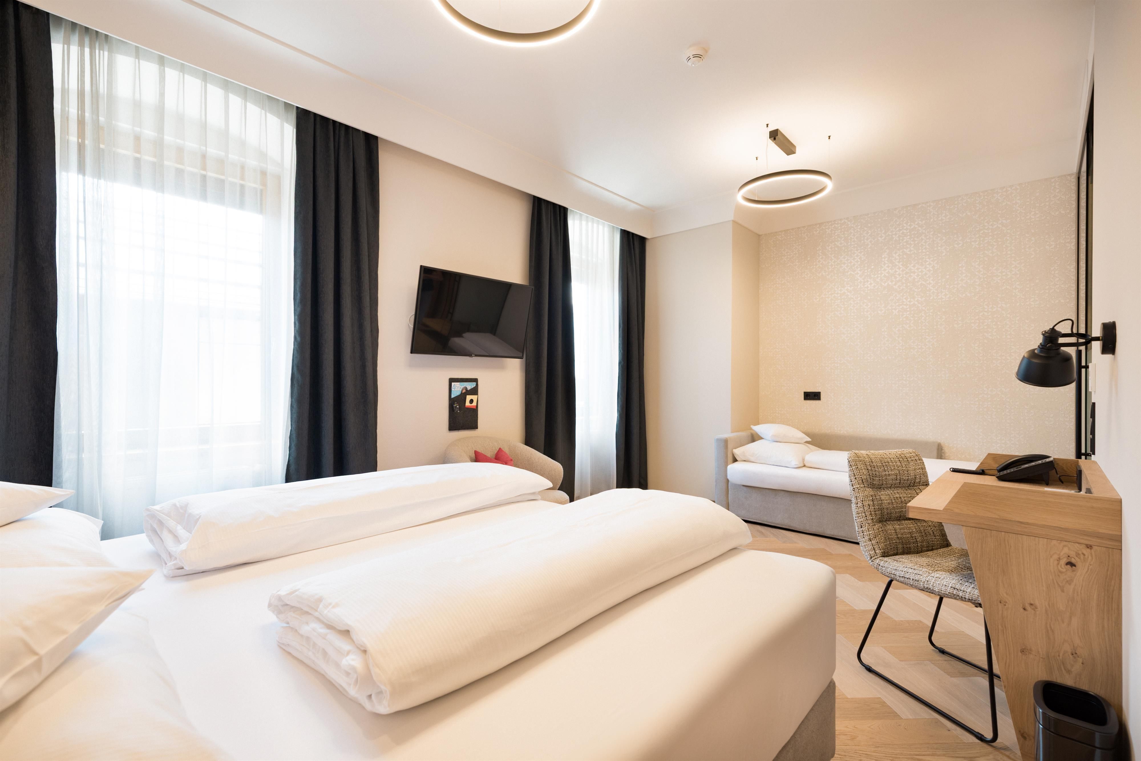 A modern hotel room with two beds, a desk, and a television. Bright curtains create a friendly atmosphere.