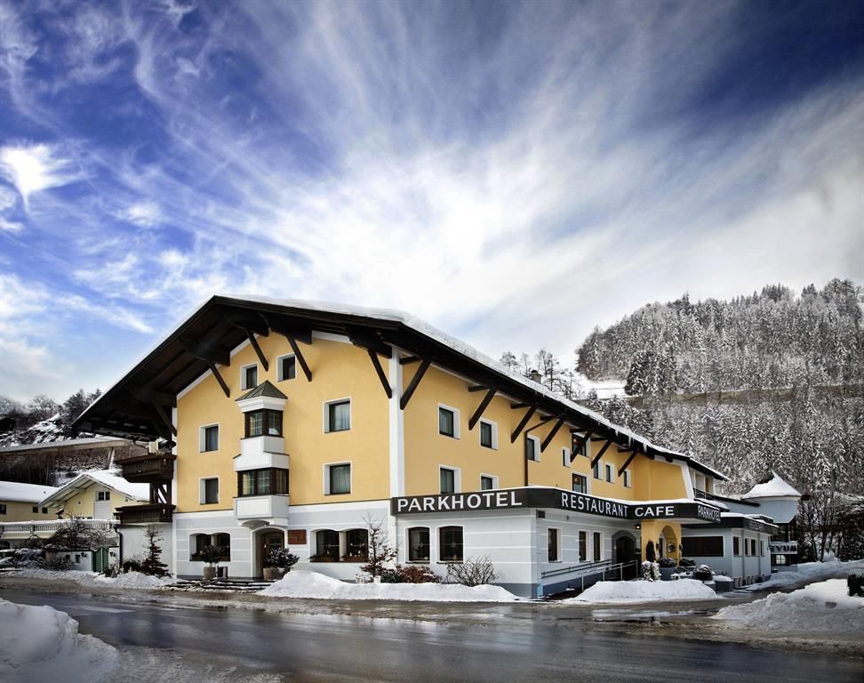 A charming park hotel with a yellow facade in winter. The surroundings are covered in snow and the clouds in the sky are dramatic.
