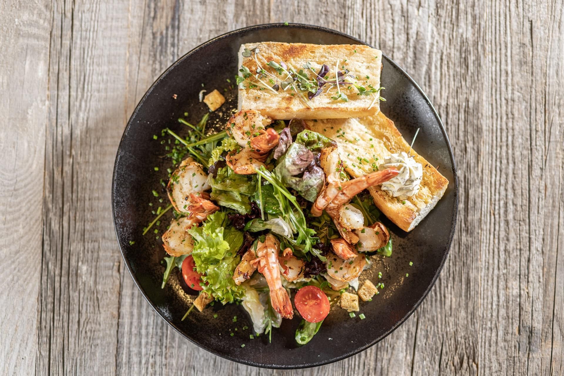 A tasty dish with shrimp, fresh salad, and two slices of toasted bread. The colors are vibrant and appealing.