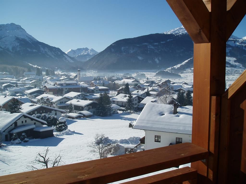 A snowy landscape with a village in the valley. Surrounded by mountains and clear blue sky.