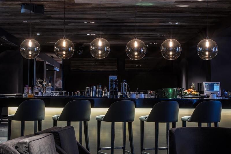 A stylish bar with modern pendant lamps and elegant chairs. The room has a dark, cozy atmosphere.