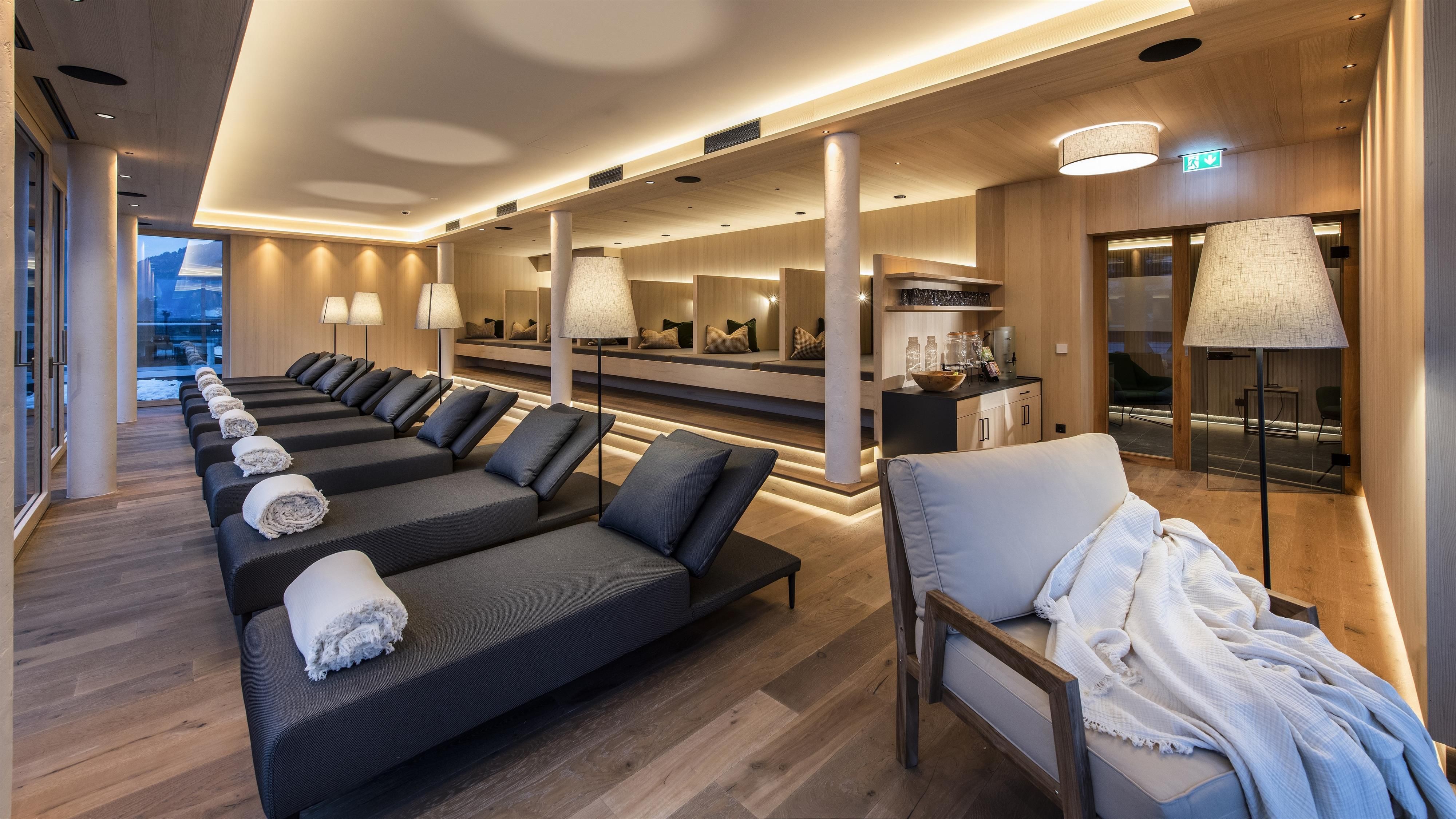 A modern wellness area with comfortable loungers and soft lighting. The wooden paneling creates a relaxing atmosphere.