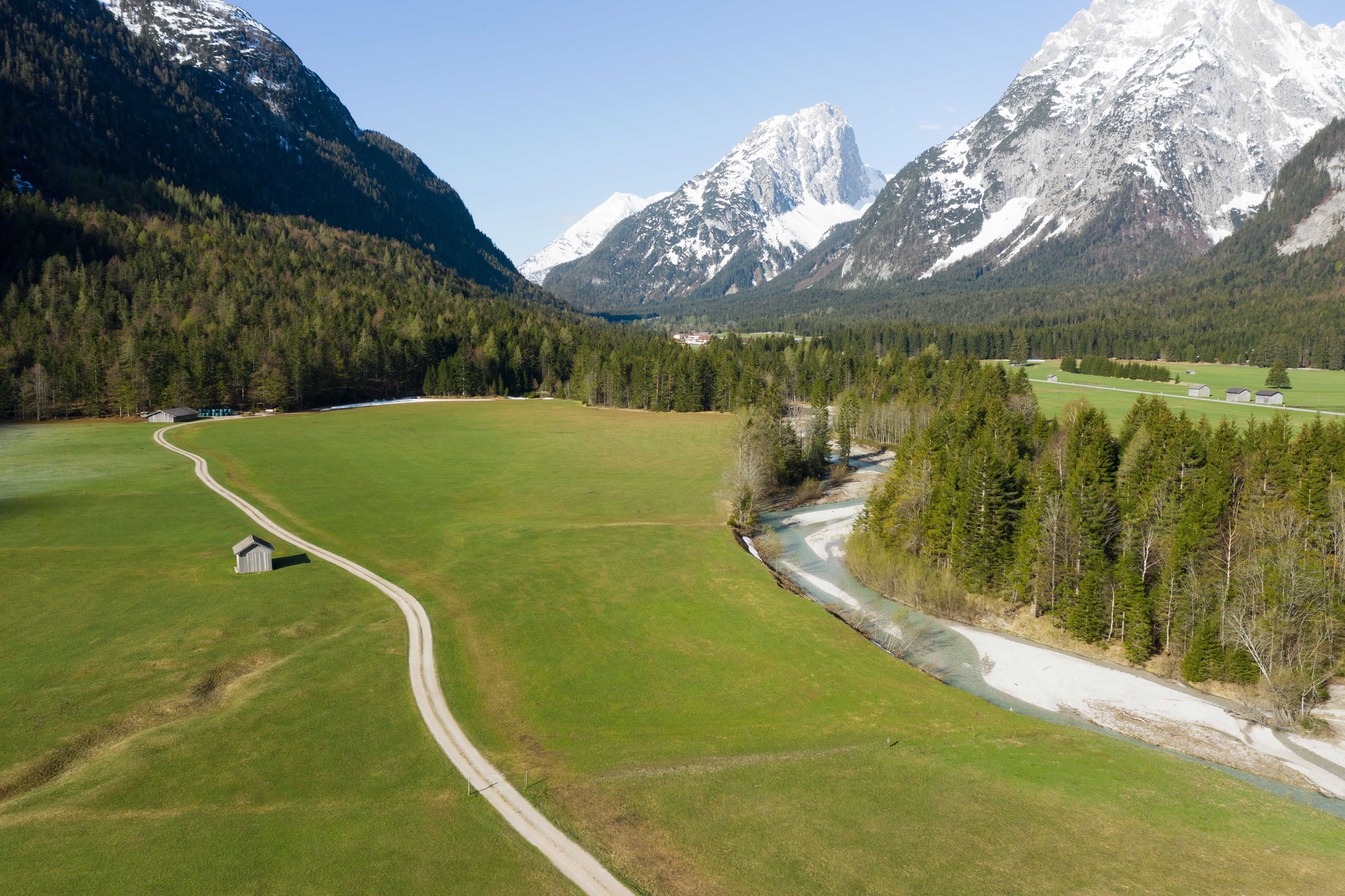 Frühling in der Leutasch, grüne Wiese und Bergbach von oben mit schneebedeckten Gipfeln im Hintergrund