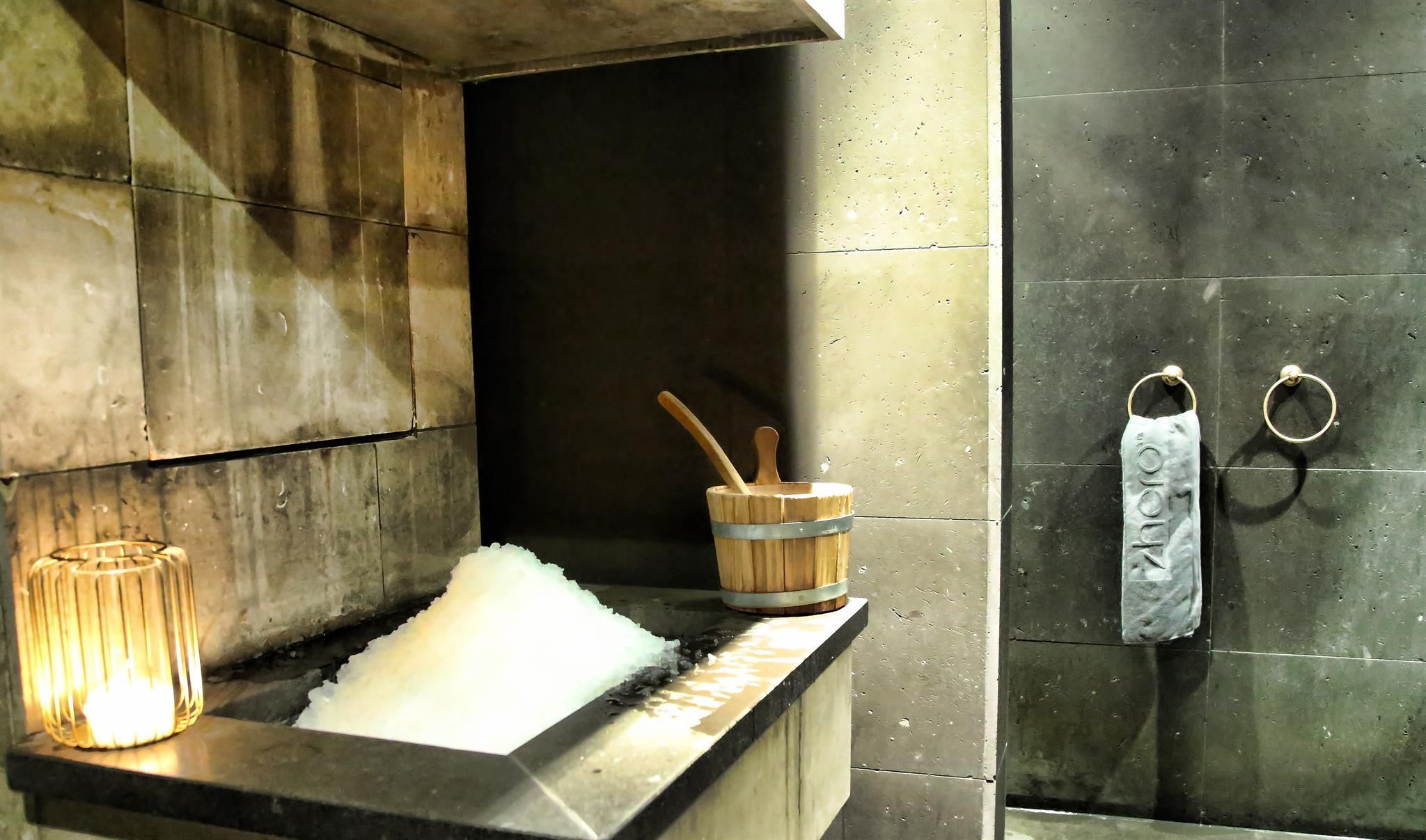 An elegant wellness area with a wooden bath and frozen water. On the wall, there is a large, dark shower wall and a towel holder.