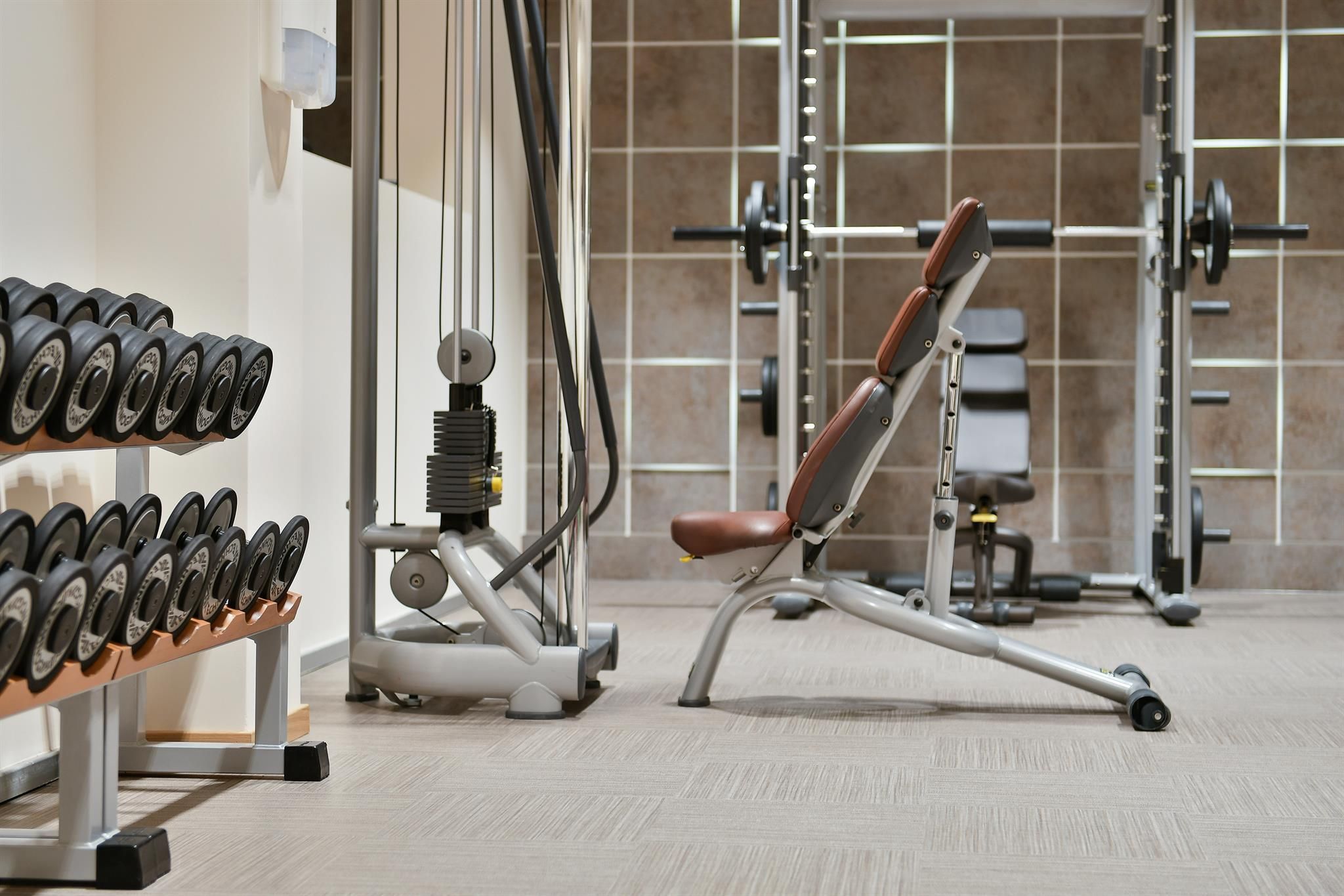 A modern gym with dumbbells and a multi-gym machine. The room is well lit and offers space for various training equipment.