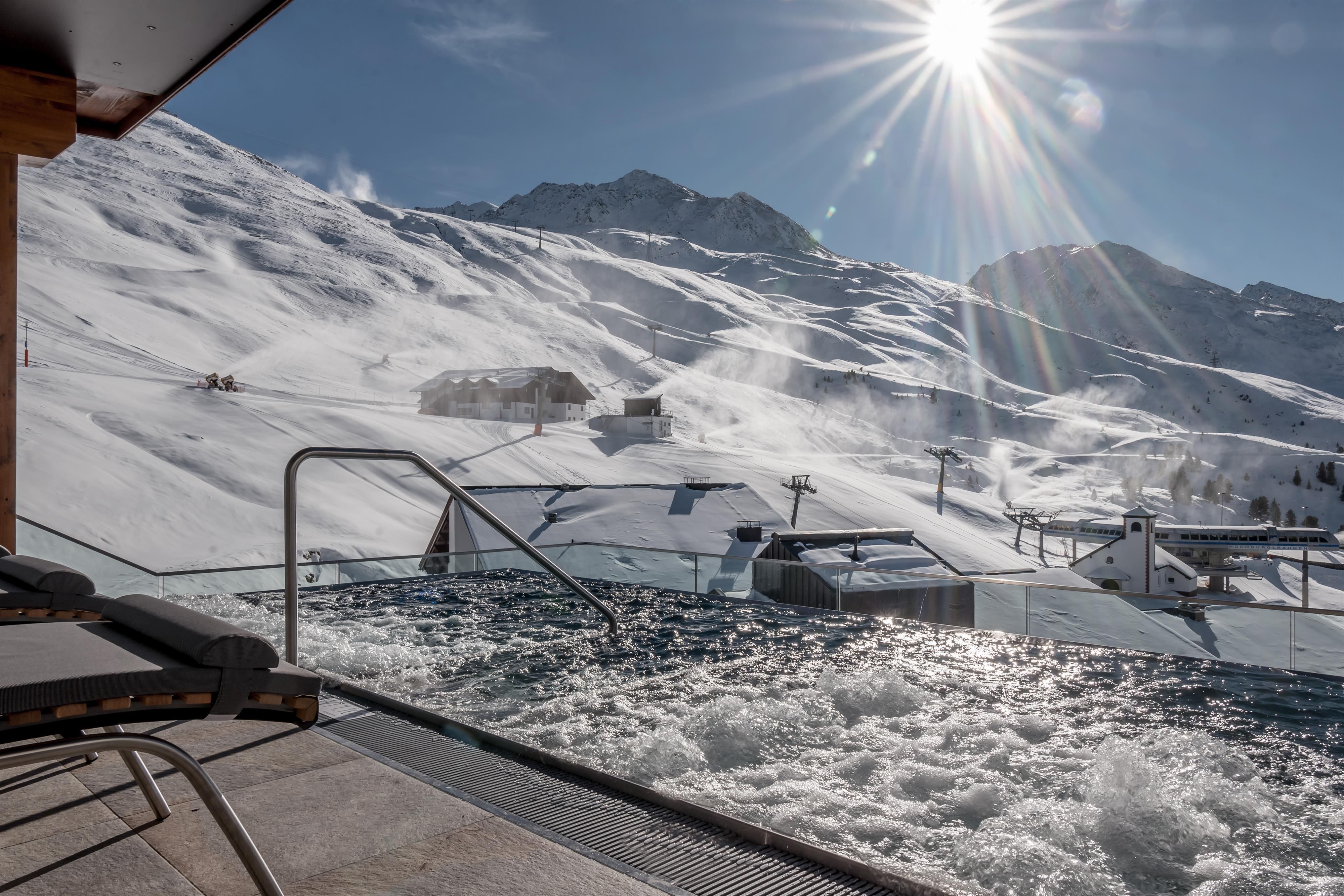 A relaxing hot tub with a view of snow-covered mountains. The sun shines over the winter landscape.