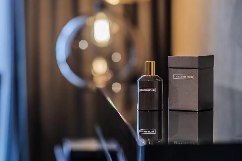 An elegant perfume bottle stands next to a stylish packaging on a glossy table. In the background, soft light sources are visible.