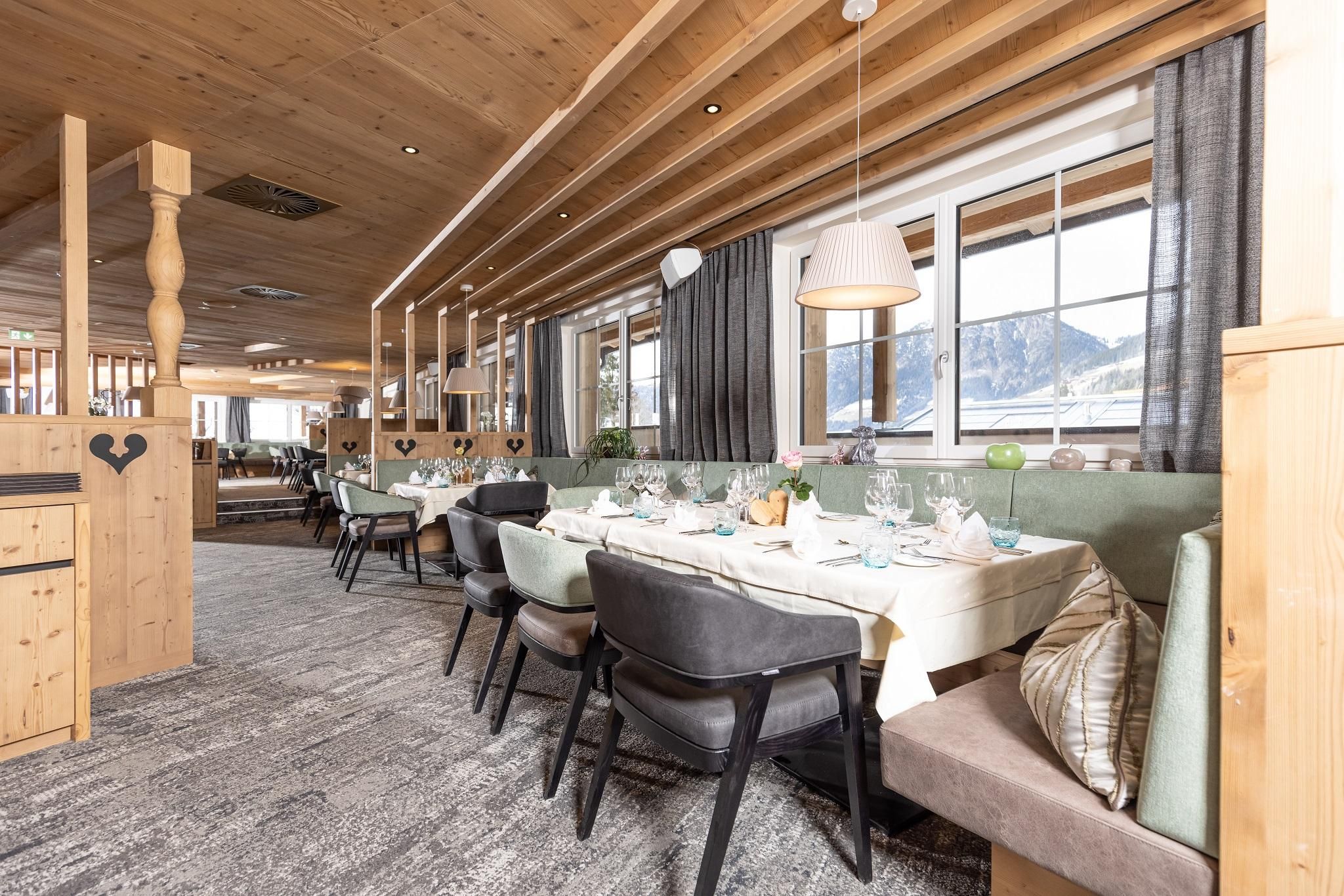 A cozy restaurant with wooden decor and elegantly set tables. Large windows provide a view of the surrounding landscape.