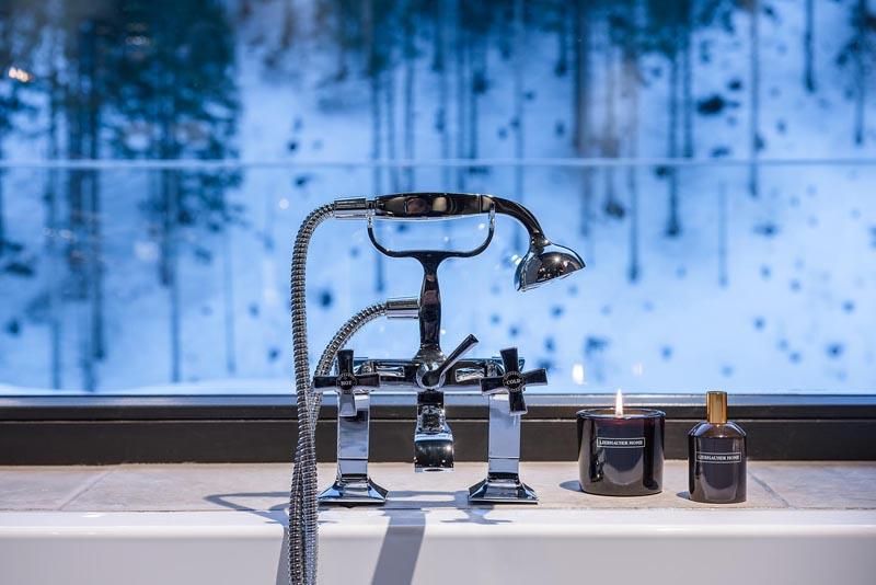 A stylish bathroom with a modern faucet and a shower. In the background, snow-covered trees can be seen through a large window.