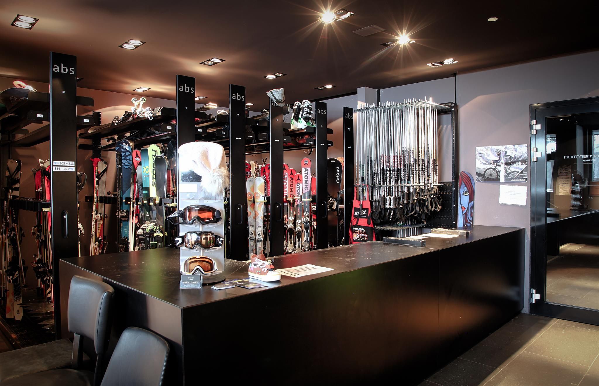 A modernly furnished ski rental with a long table and shelves full of skis and snowboards. The walls are stylishly decorated, and the lighting creates an inviting atmosphere.