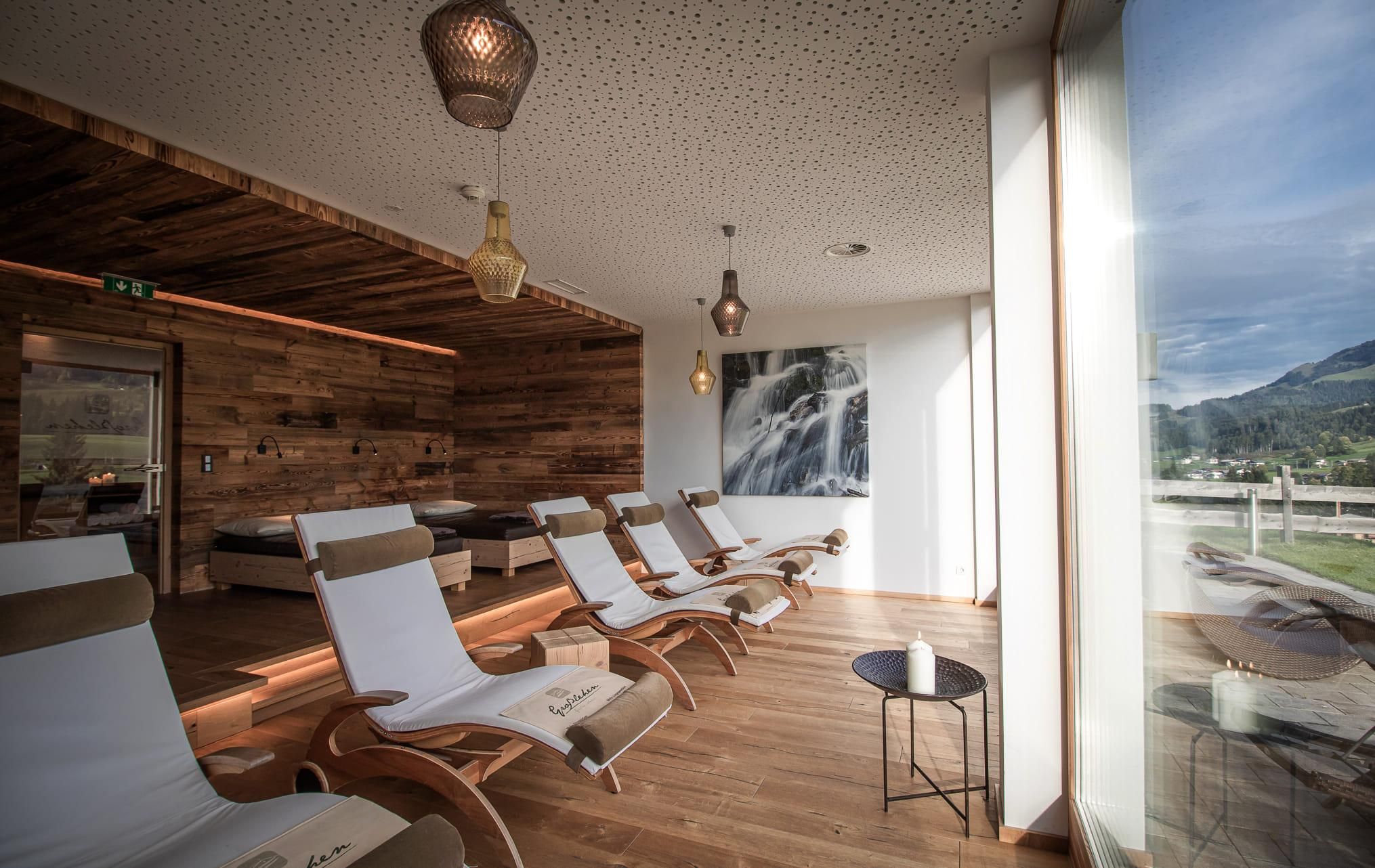 An elegant wellness area with modern loungers and warm wood design. Large windows offer a view of the surrounding nature.
