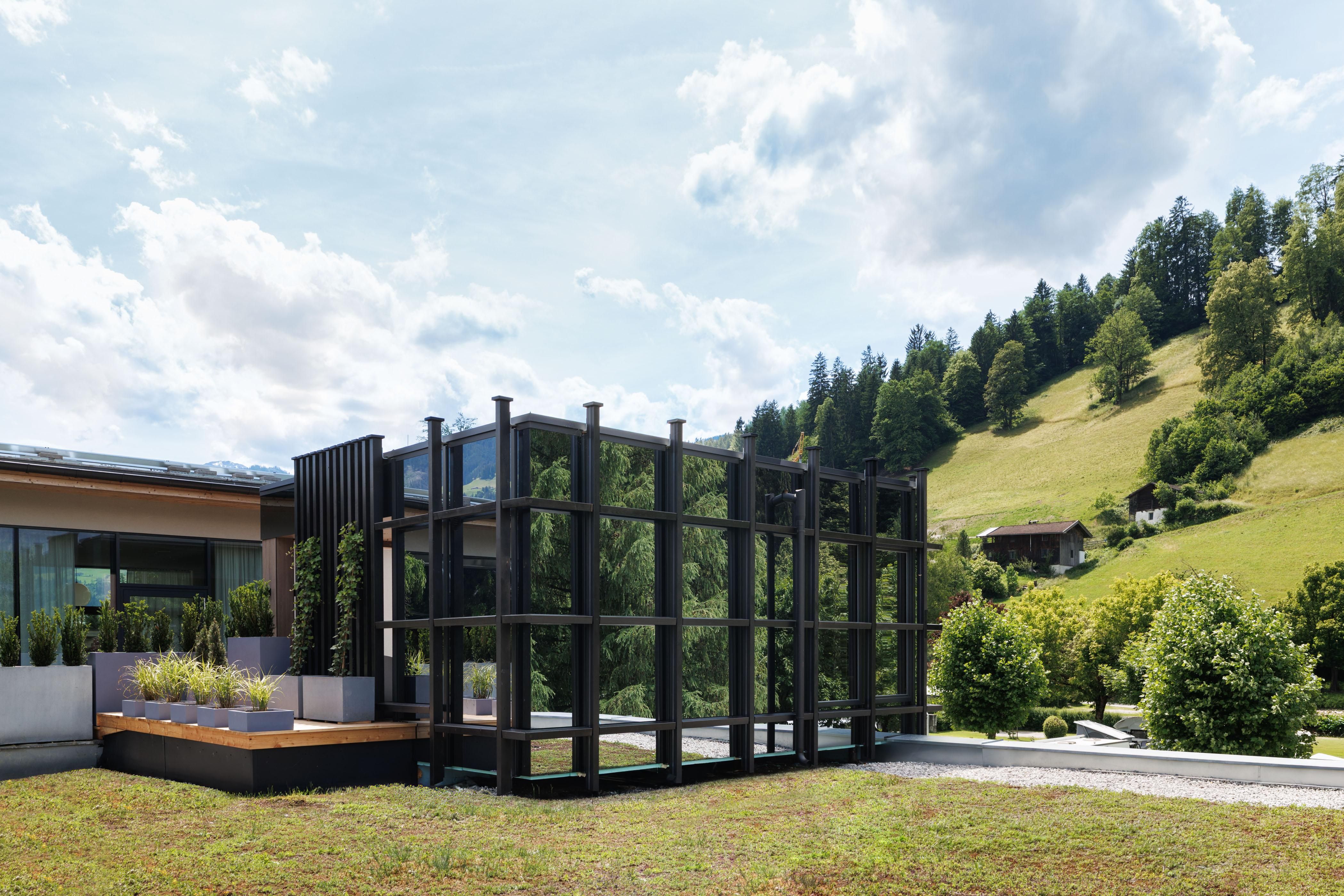 A modern building with large glass surfaces and a stylish outdoor area. In the background, green hills and trees can be seen.