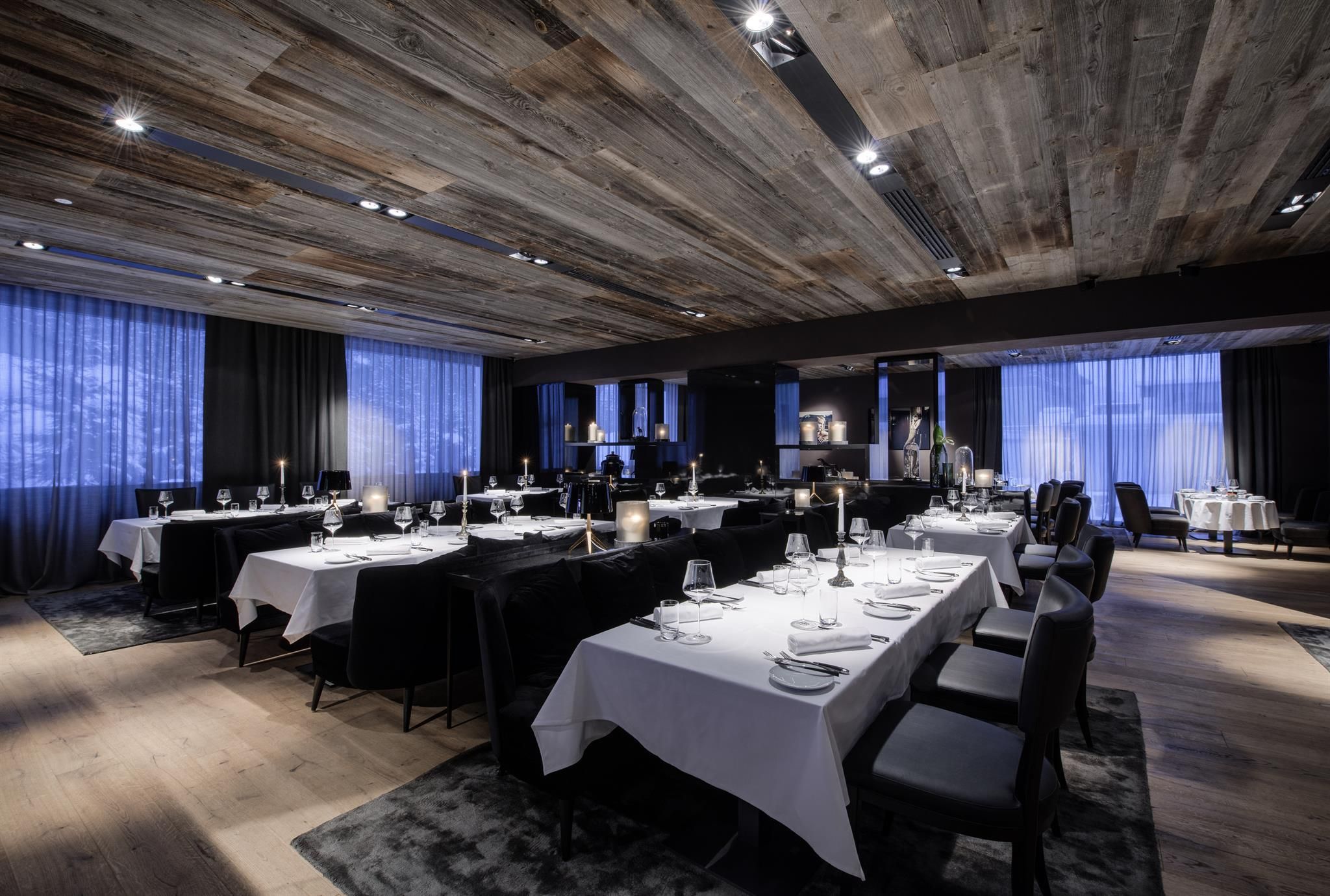 An elegant restaurant with set tables and a modern atmosphere. Large windows let in soft light.