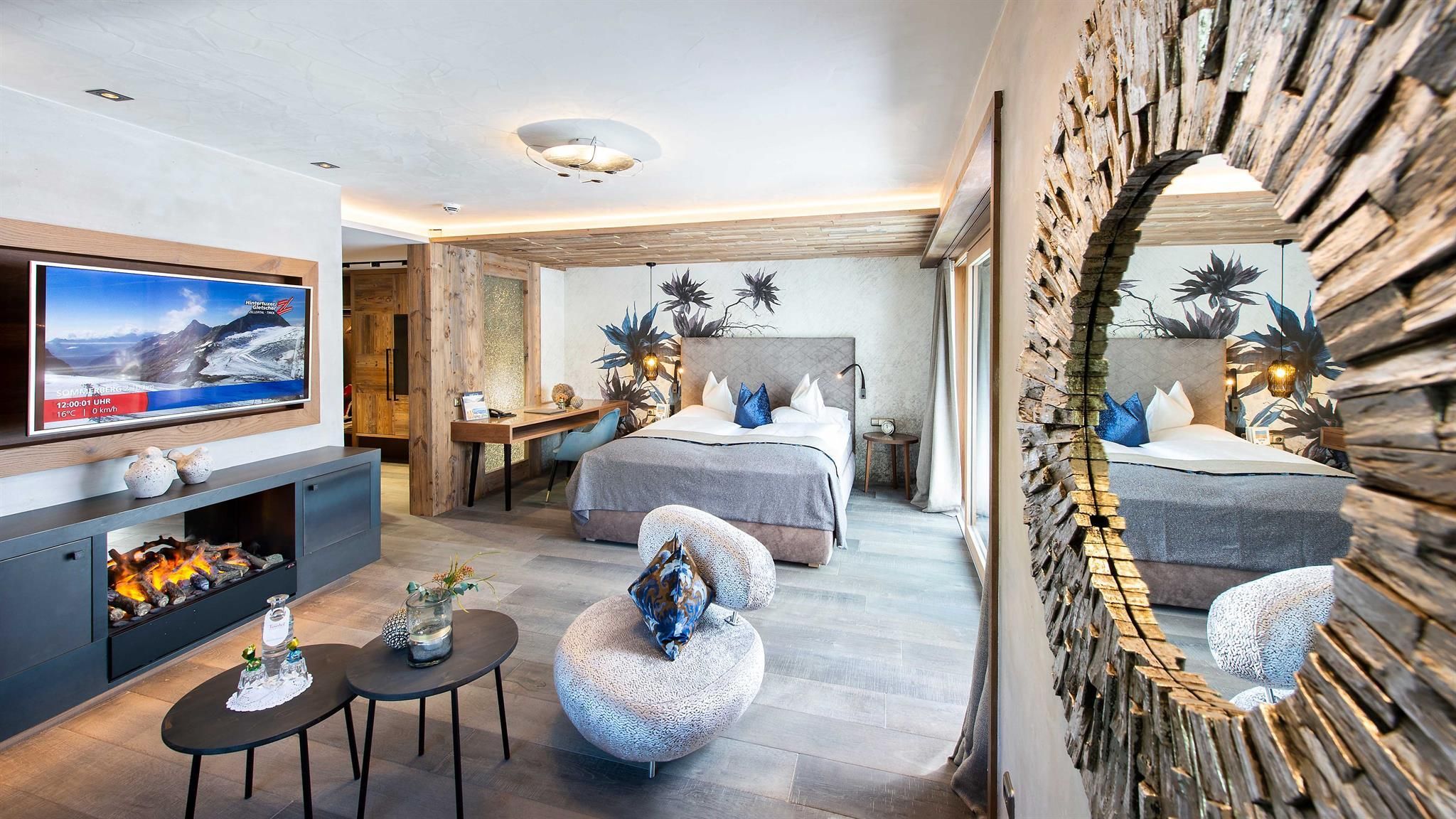 A modern bedroom with a large bed and a flat-screen TV. The decor is stylish and includes a cozy seating area as well as a brightly lit atmosphere.
