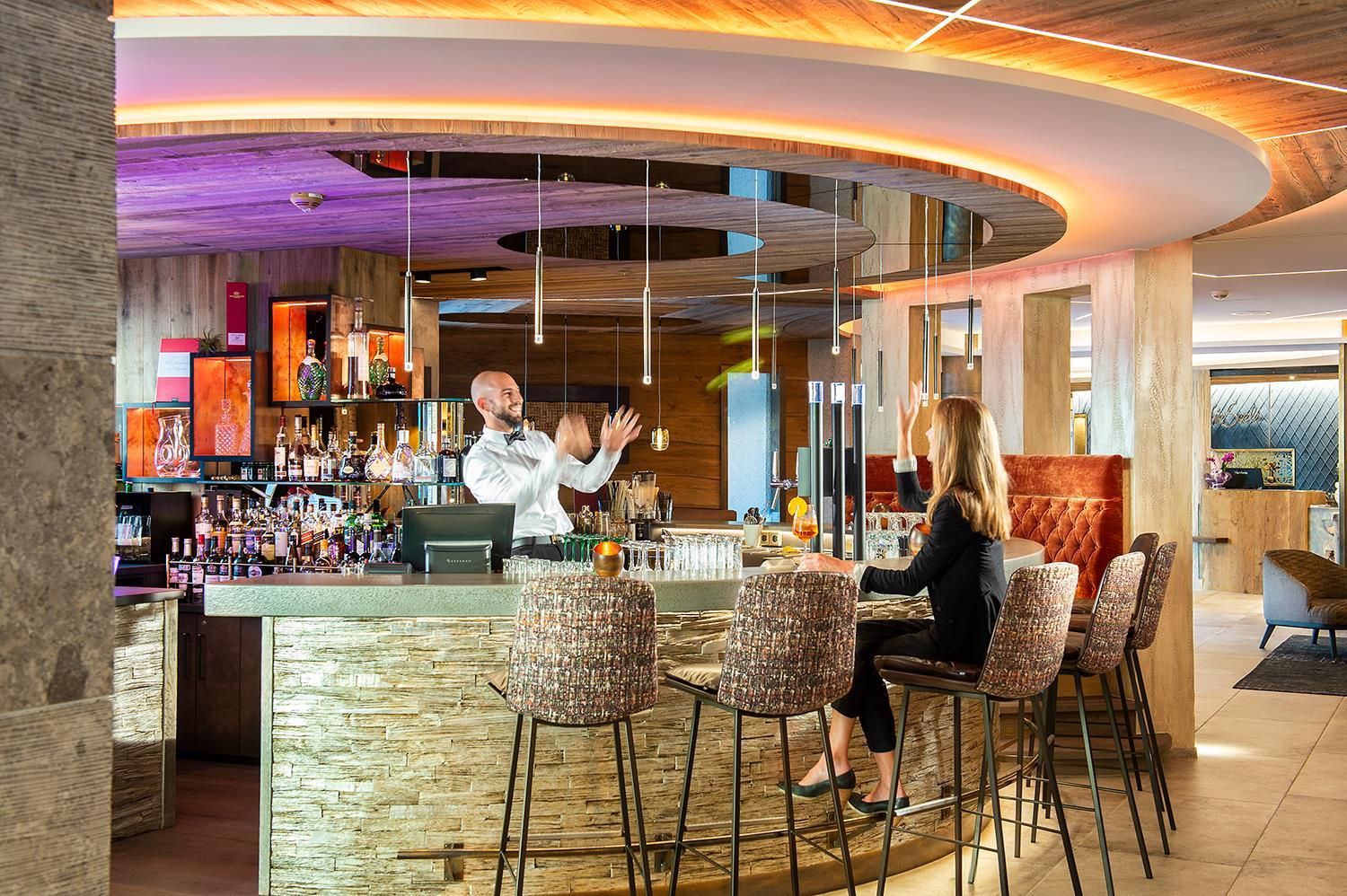 A stylish bar with a bartender preparing drinks. A woman is sitting at the bar and watching him.