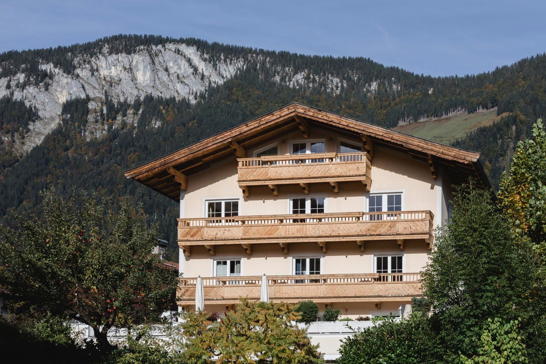 A charming house in alpine style with wooden decorations. In the background, majestic mountains and green terrain can be seen.