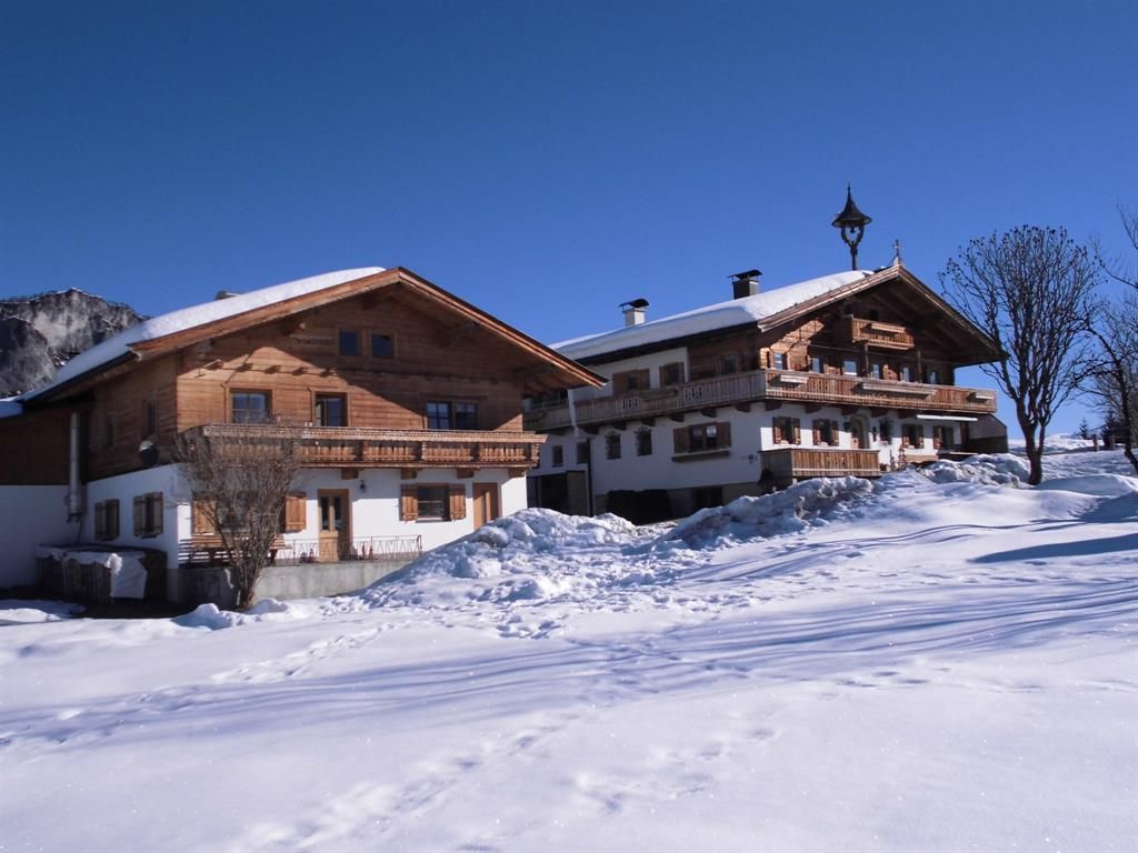 Two traditional huts in the snow, surrounded by a clear blue sky. The landscape is wintry and inviting.