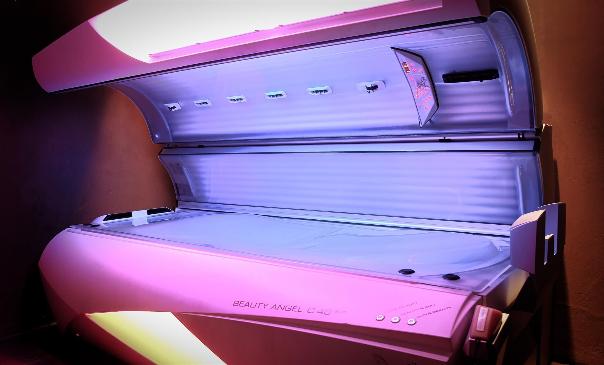 A modern tanning bed device with soft purple lighting elements. It has a large lying surface and a comfortable design for tanning applications.