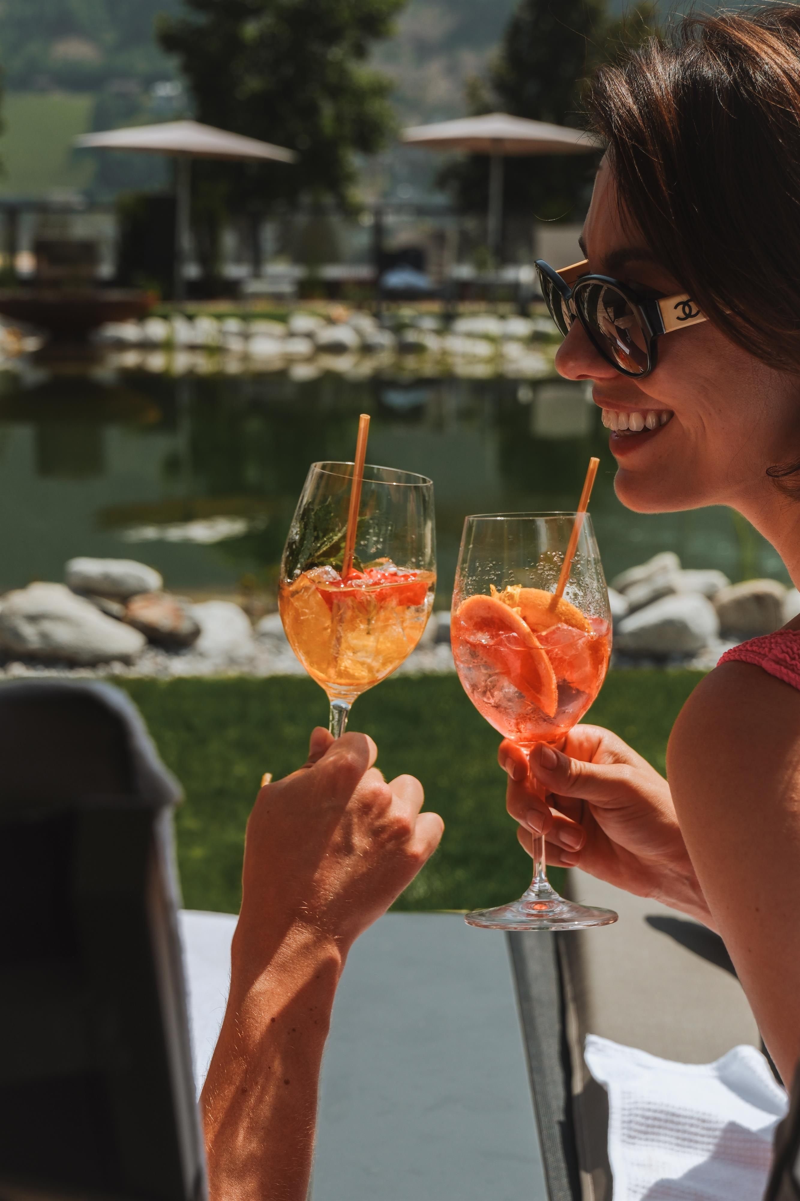 A woman enjoys refreshing drinks by the pond. The mood is relaxed and sunny.