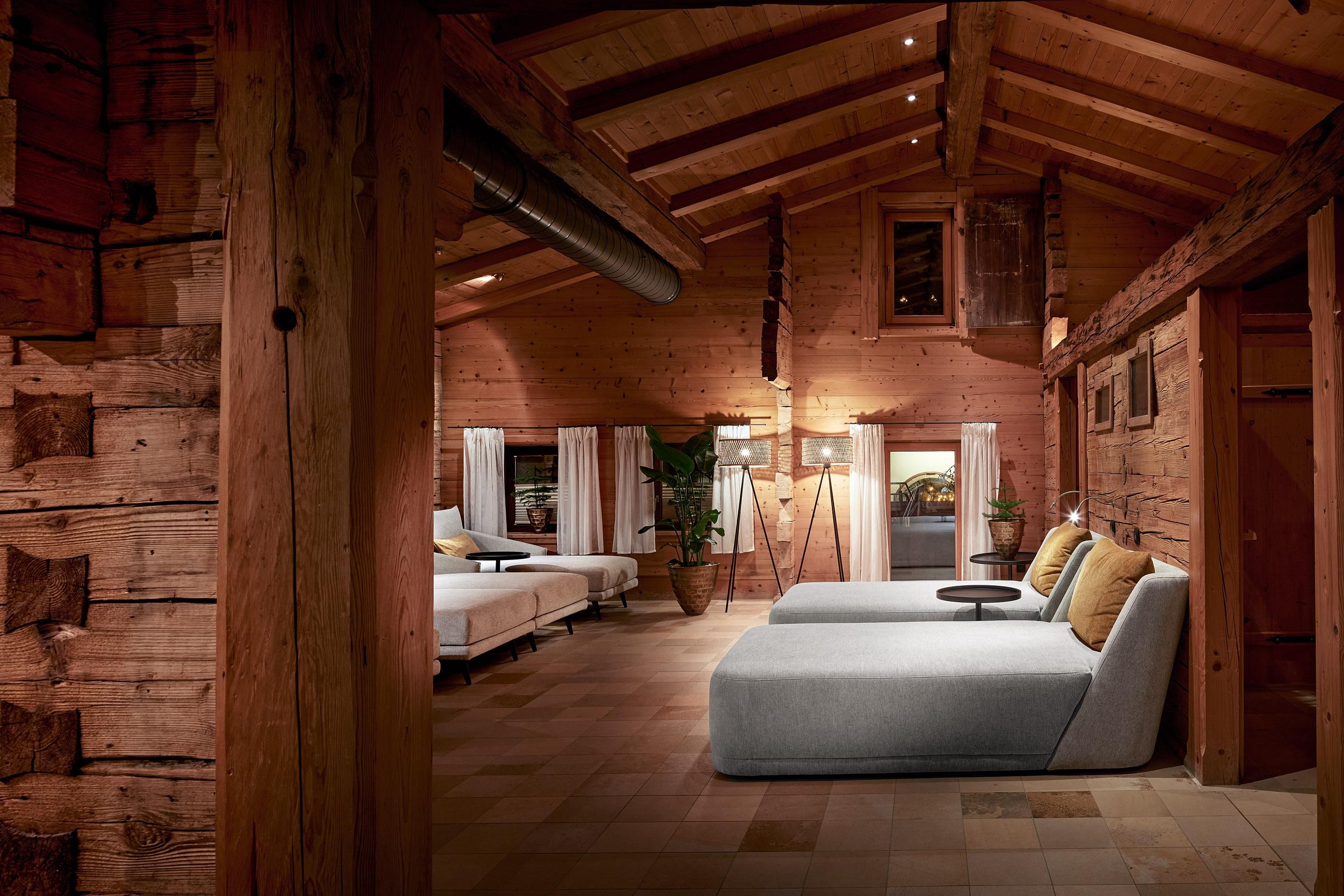 A cozy room with wooden walls and a high ceiling beam. Two comfortable loungers and modern lighting create a relaxed atmosphere.