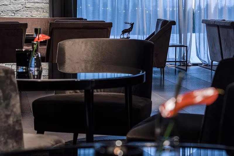 A stylish café with elegant black chairs and tables. In the background, soft curtains and a decorative figure are visible.