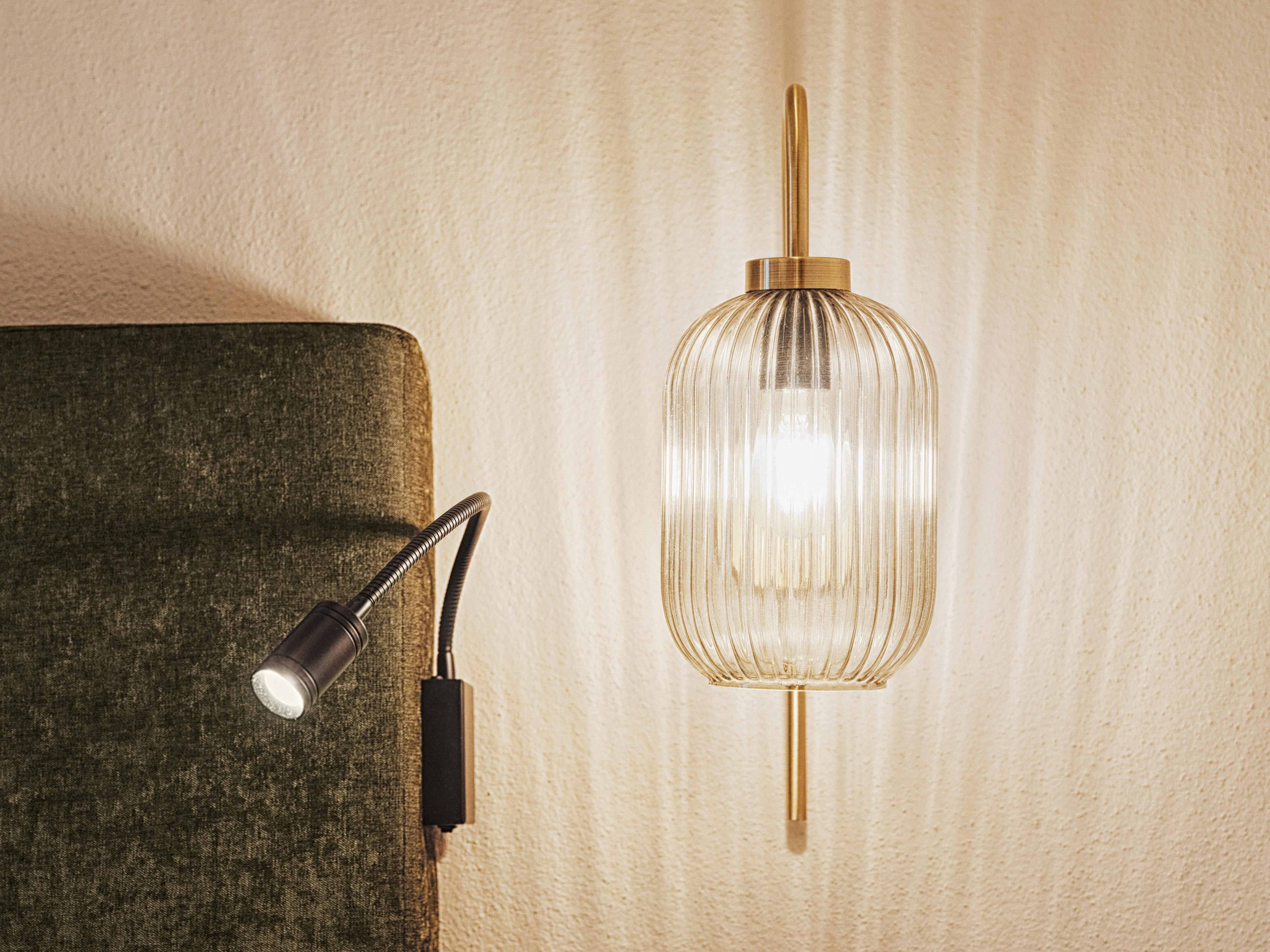 A stylish wall lamp with an elegant, ribbed design softly illuminates. Next to it is a flexible reading lamp for additional light.