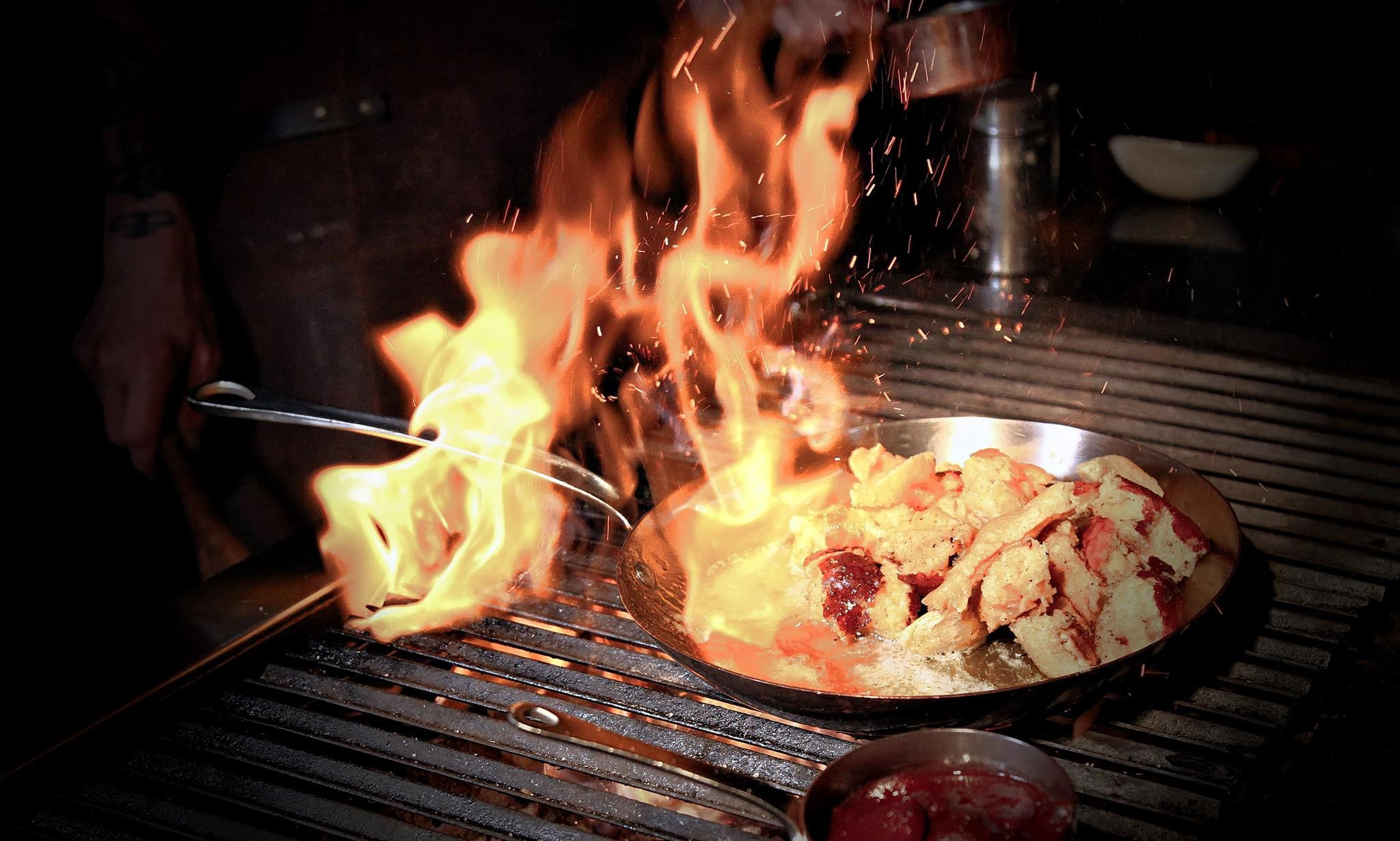 A dish is flambéed while it is being prepared on a grill. Flames surround the food, creating an impressive presentation.