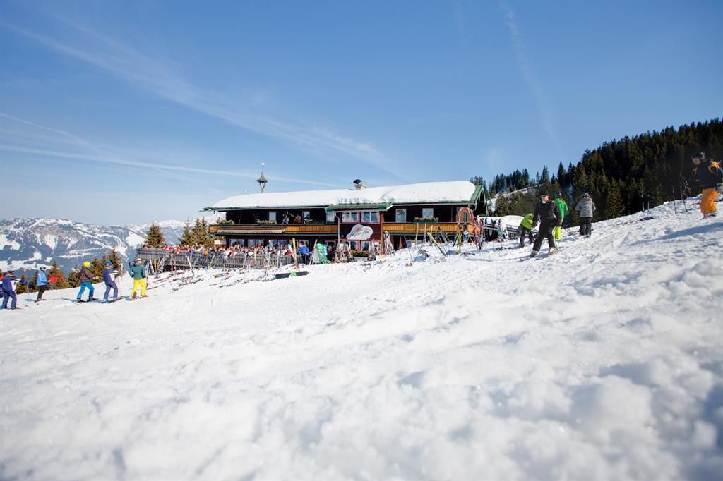 A snow-covered winter landscape with a ski lodge in the background. Ski slopes and skiers are visible in the foreground.