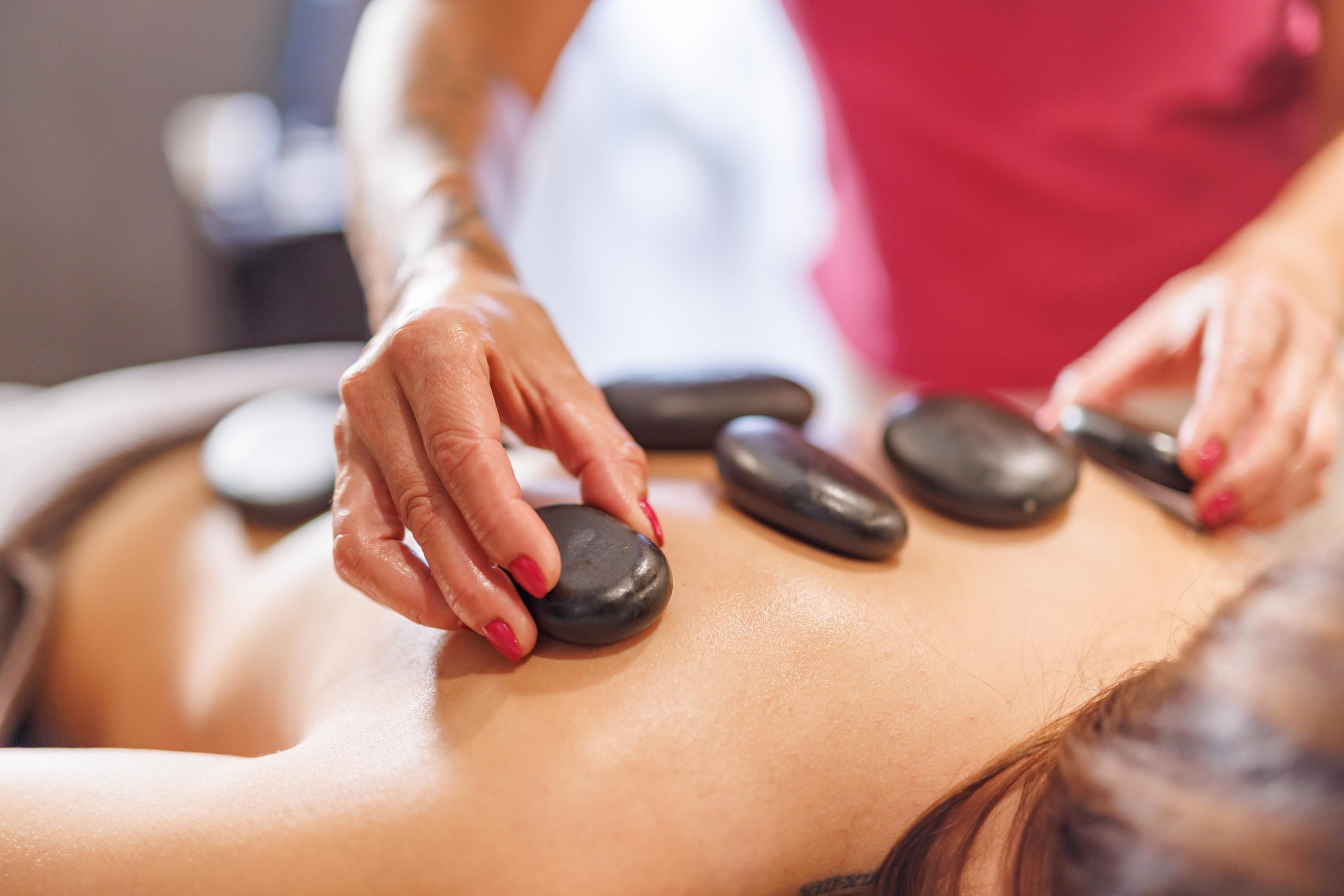 A relaxing massage with hot stones on a person's back. The therapist carefully places smooth, black stones for the treatment.