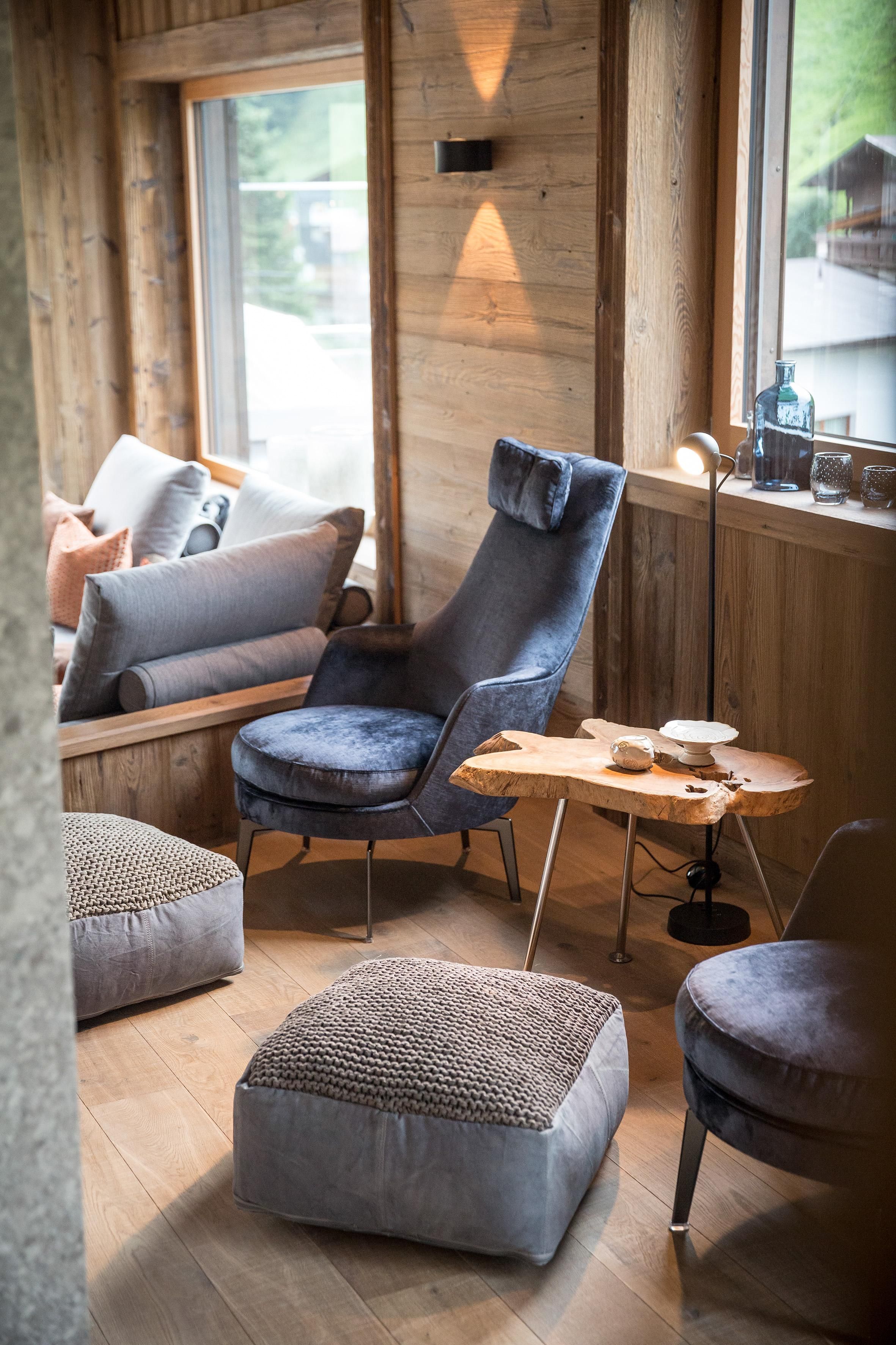 A cozy lounge area with modern armchairs and a small wooden coffee table. The room has large windows and a warm, inviting atmosphere.