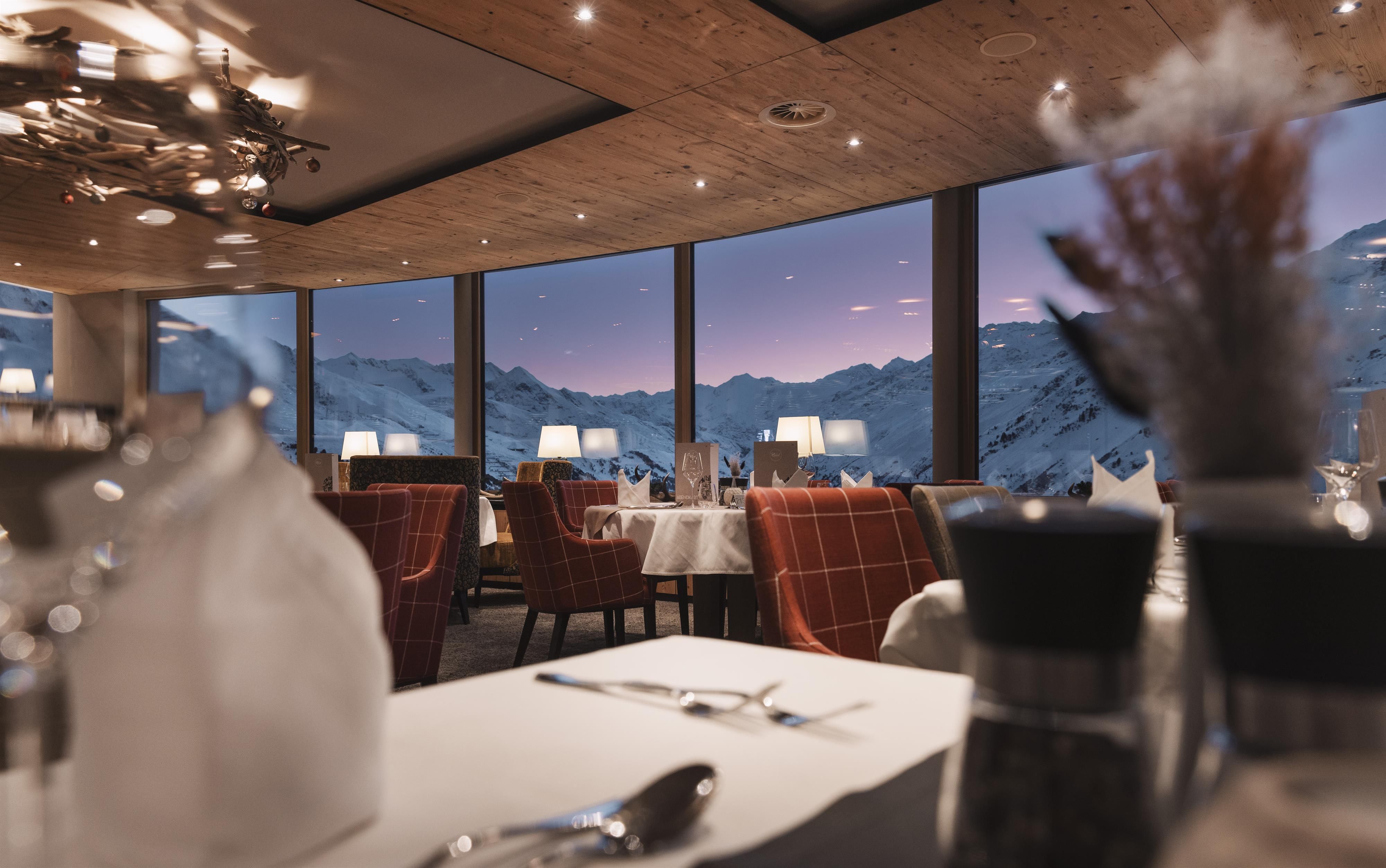 An elegant restaurant with large windows and a view of the mountains. The modern interior design creates a warm and inviting atmosphere.