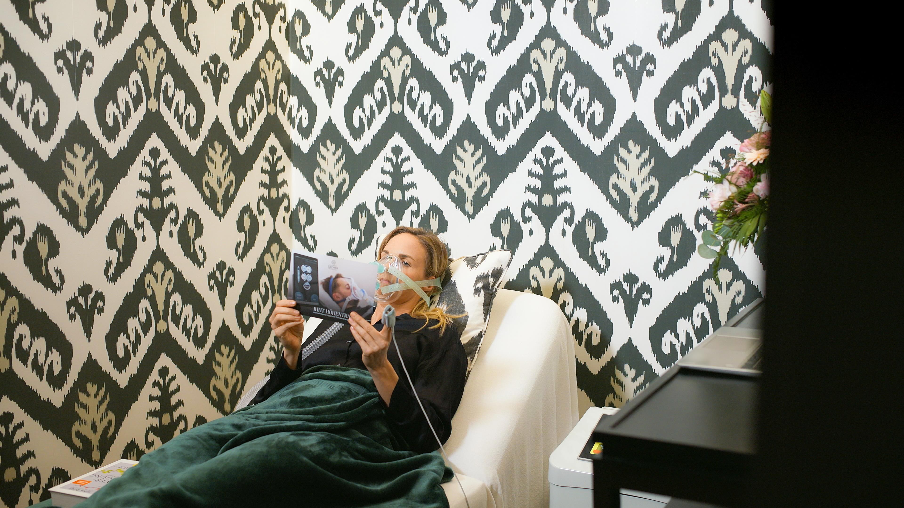 A woman is lying on a sofa and reading a magazine. The background is decorated with a striking graphic pattern.