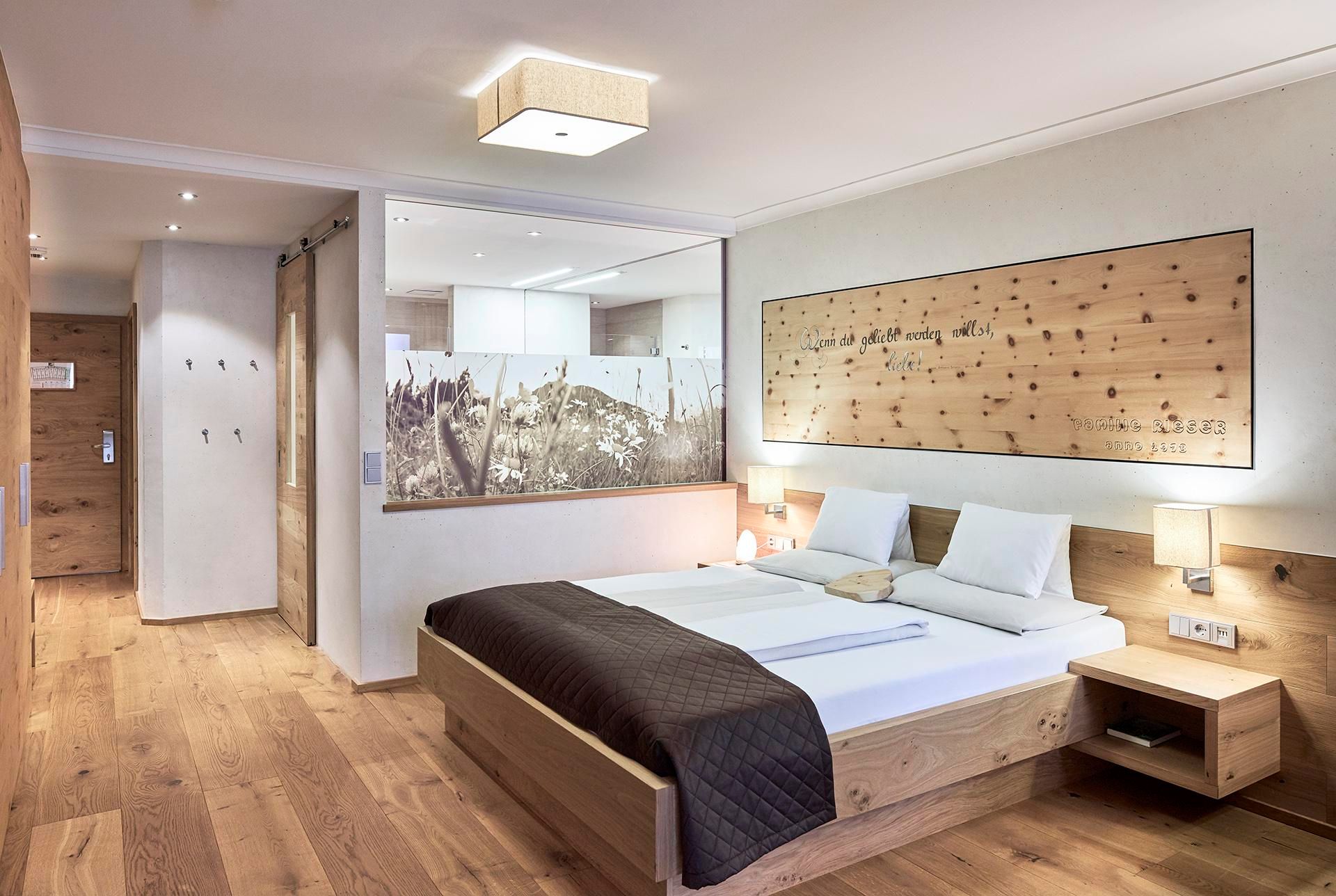 A modern bedroom with wood decor and a large window. The furnishings are bright and inviting, featuring a double bed and nightstands.