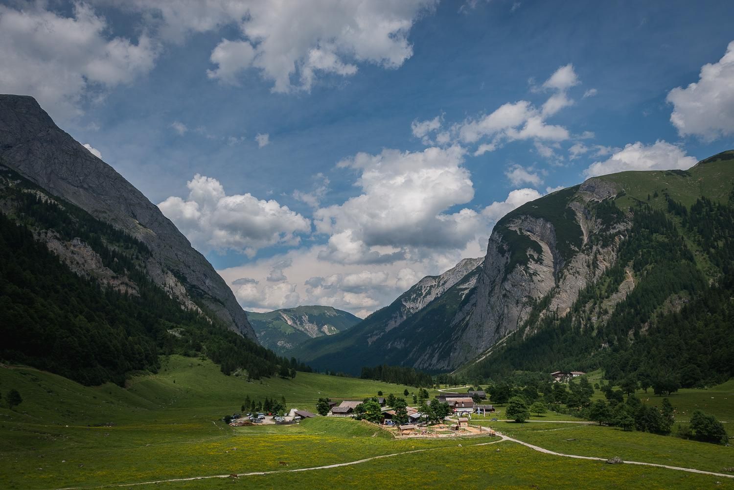 A picturesque mountain landscape with green meadows and majestic rocks. The sky is clear with a few clouds.