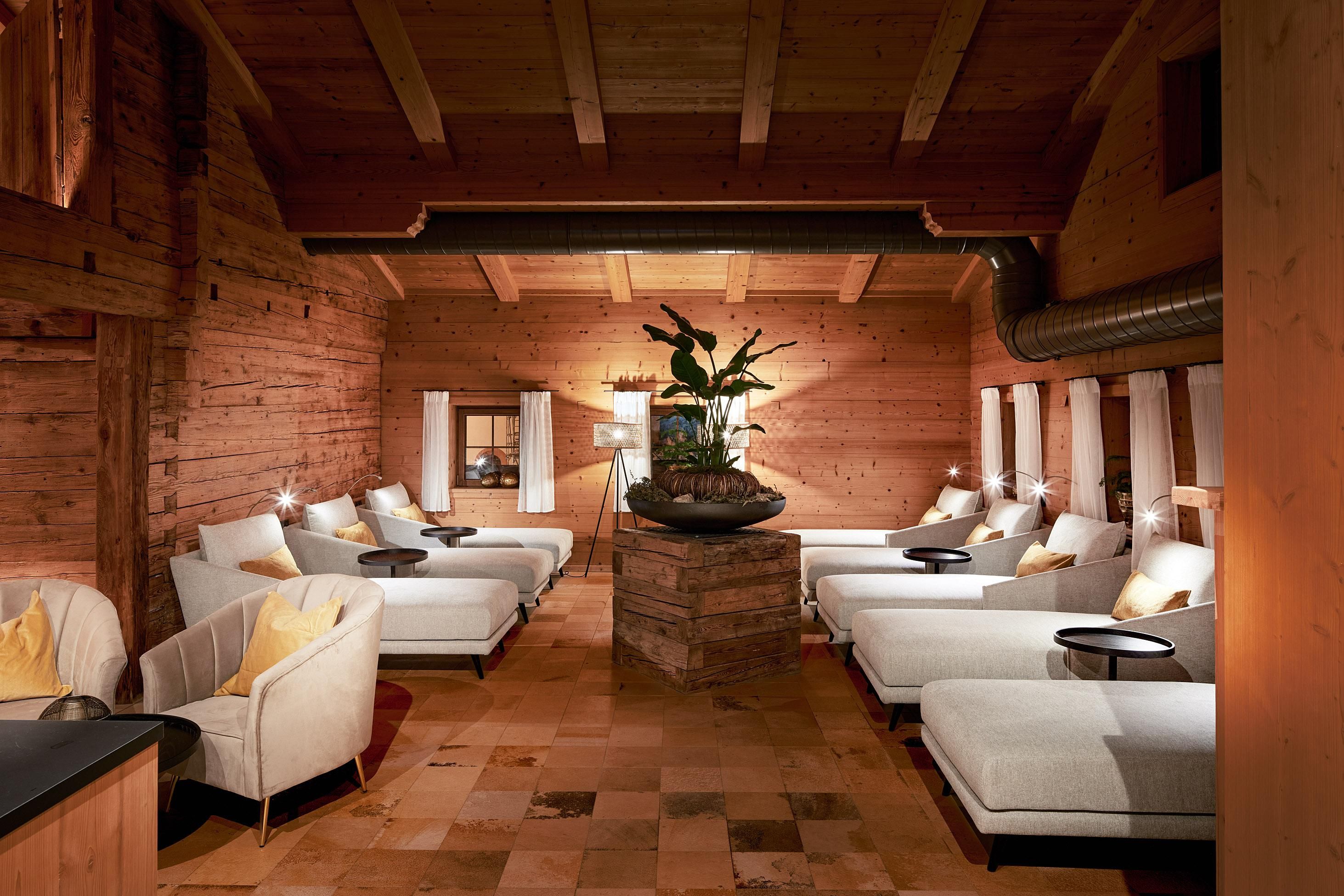 A relaxing wellness room with comfortable loungers and wooden paneling. In the center, there is a decorative water basin with plants.