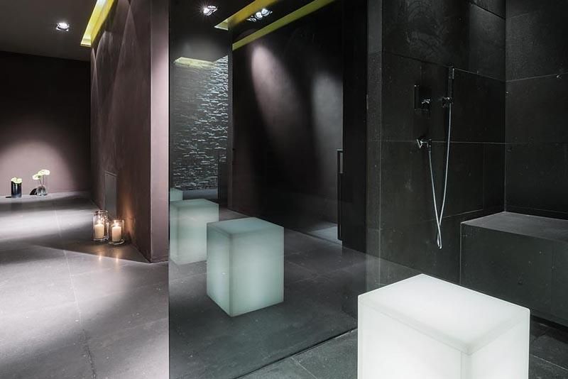 A modern bathroom with dark walls and elegant design elements. White, luminous cubes create a sophisticated atmosphere.