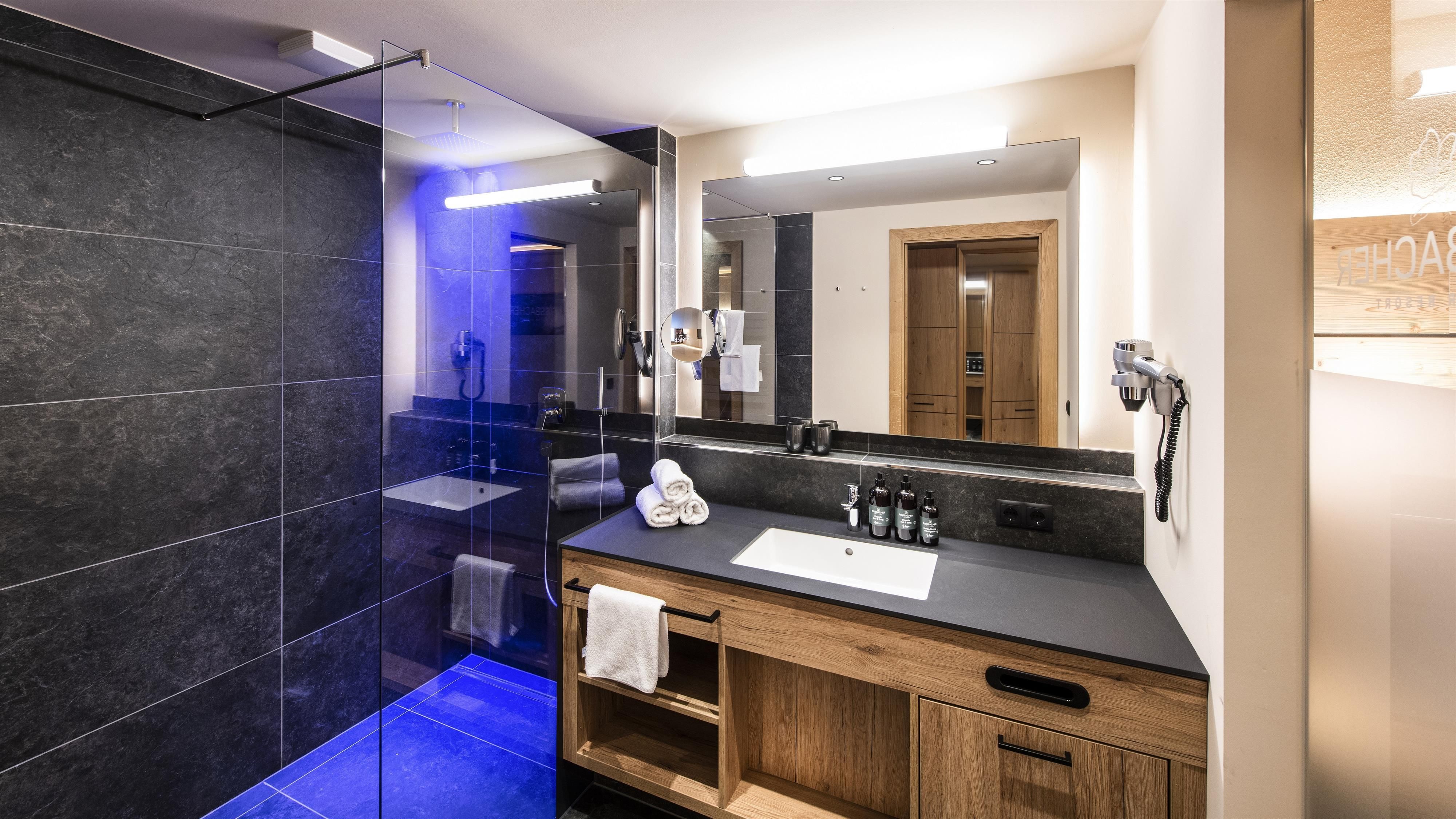 A modern bathroom with a glass shower and a stylish wooden vanity. The walls are in dark granite, giving an elegant look.