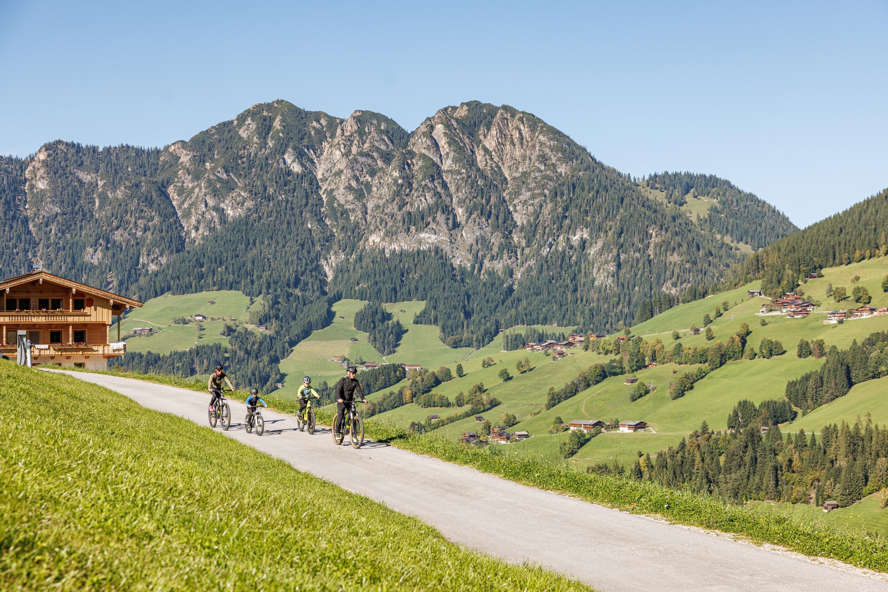 A group of bike cafes stands on a road in the mountains. In the background, green meadows and majestic mountains can be seen.