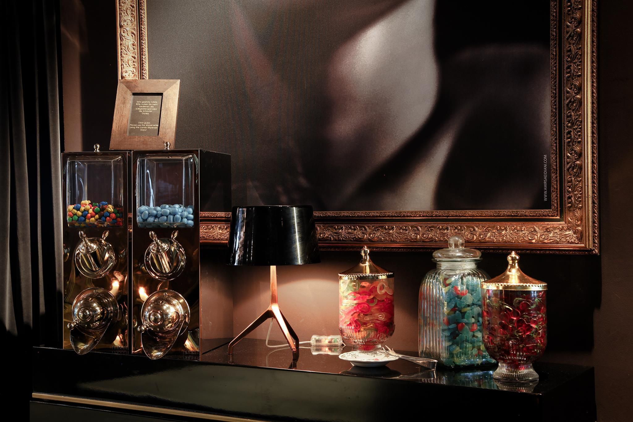 A stylish arrangement of candies in jars, complemented by an elegant lamp. In the background, there is a piece of artwork in a golden frame.