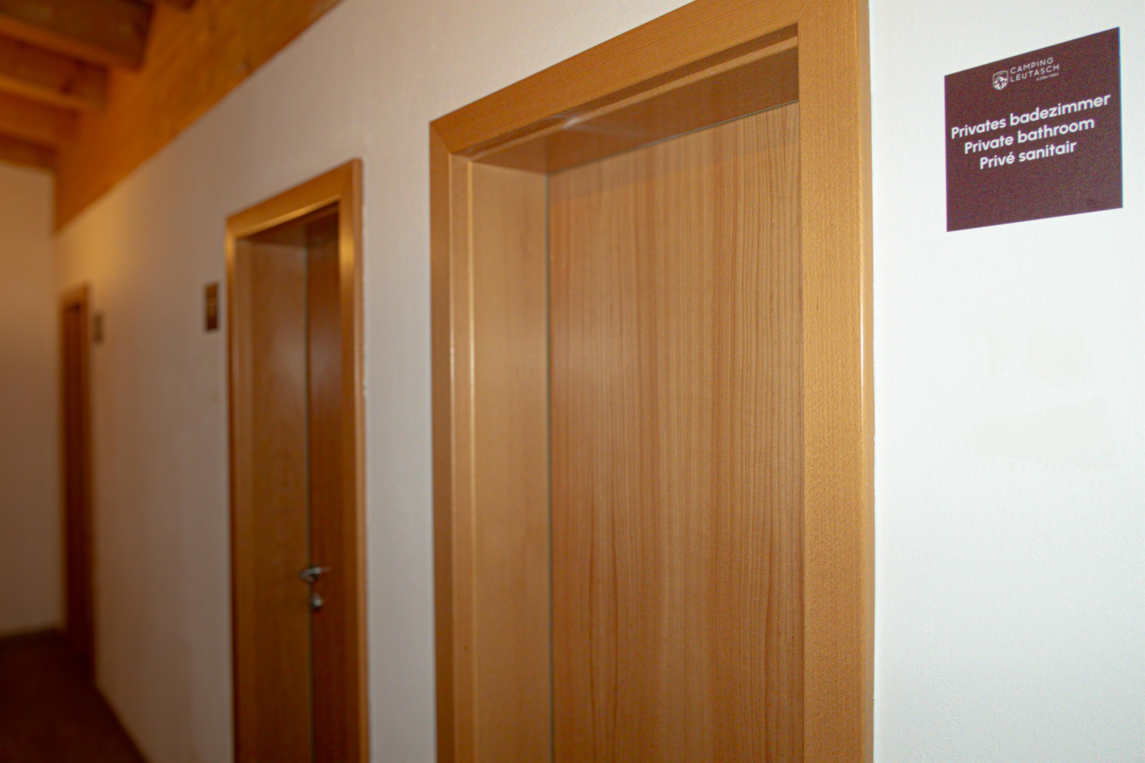A hallway with several wooden room doors. A sign with information about a bathroom hangs on the wall.